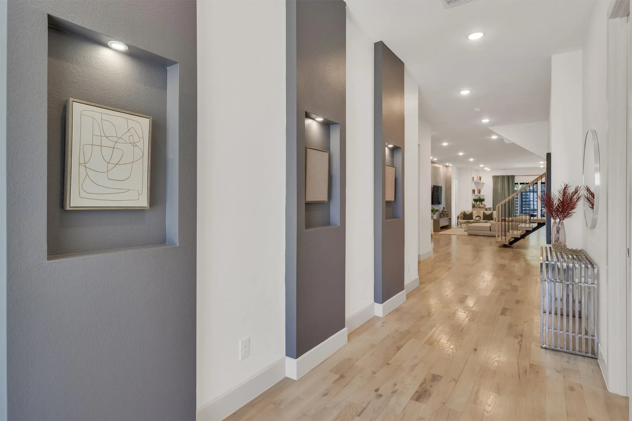 Recessed wall niches with accent lighting, high ceilings with recessed lighting, wood-finish flooring, and a visible staircase with wood newel posts