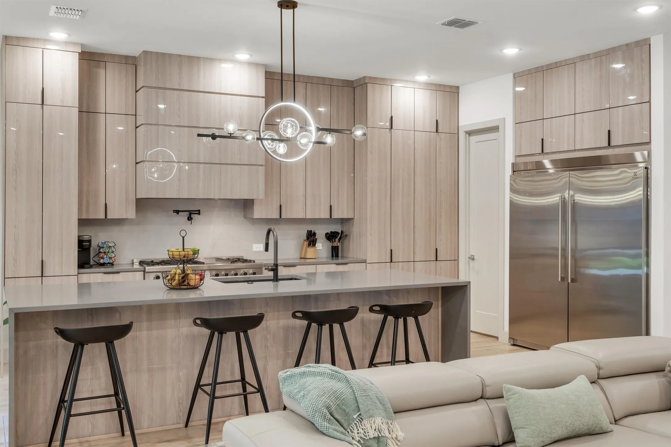 Modern kitchen featuring light wood-finish cabinetry, stainless steel appliances, a light-toned countertop, and an integrated kitchen island with seating