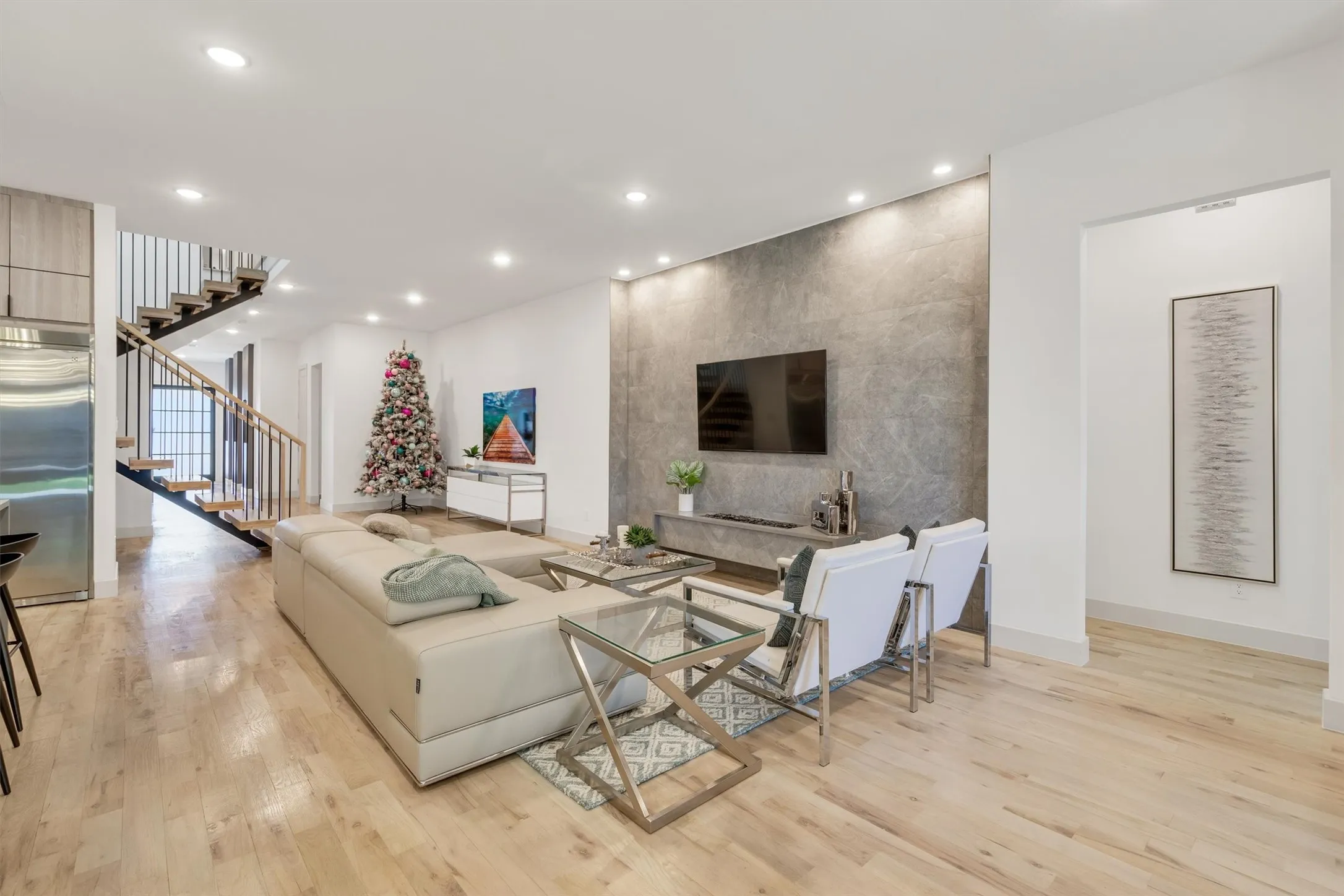 Open-concept living area featuring wood-finish flooring throughout, recessed ceiling lighting, and a textured accent wall with mounted flat-screen television