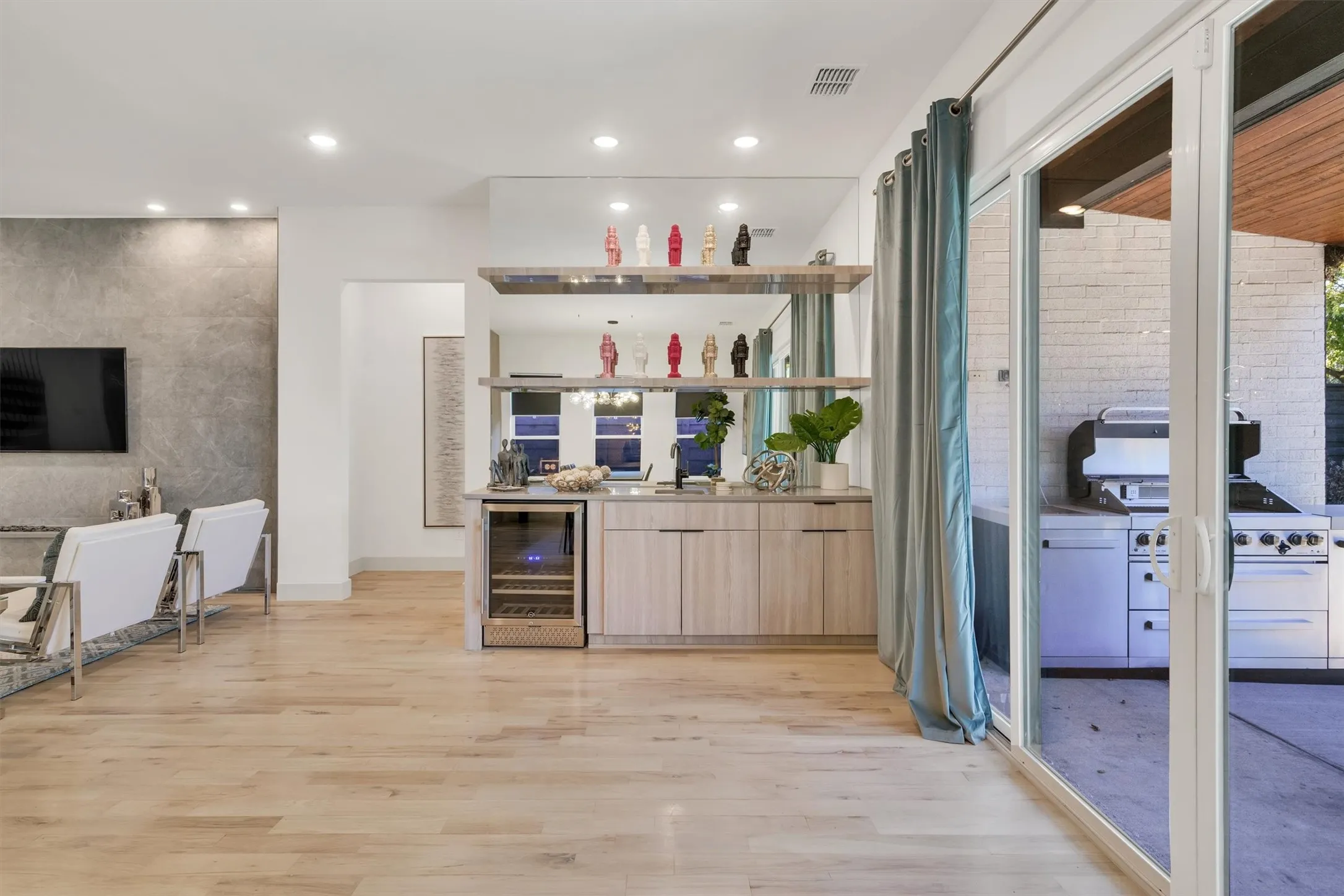 Open-concept living area featuring wide-plank wood-finish flooring, recessed ceiling lighting, and a custom built-in beverage bar with glass-front refrigeration, open shelving, and warm wood cabinetry