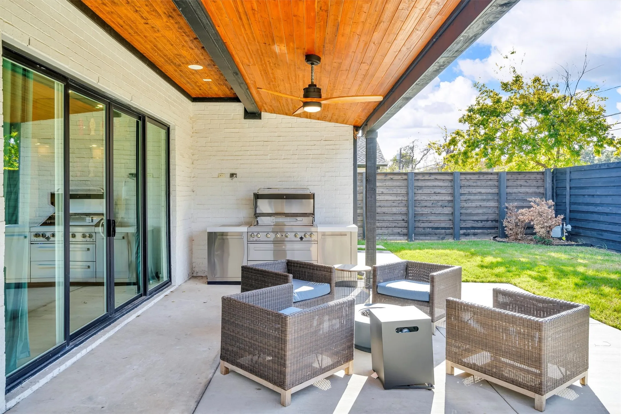 Covered patio featuring a wood-panel ceiling, built-in outdoor kitchen with stainless steel appliances, and a privacy fence