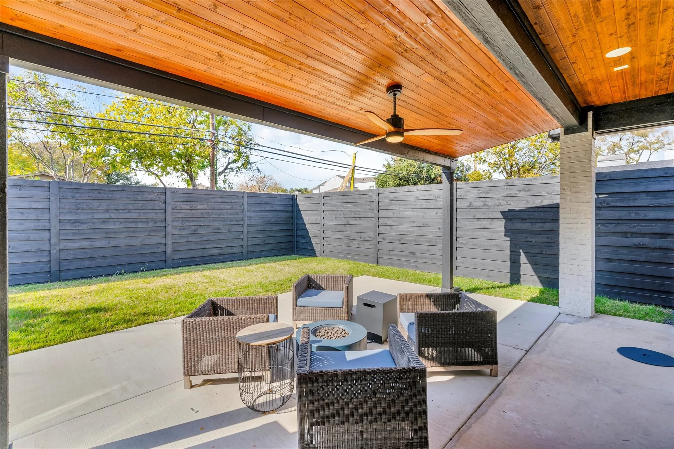 Covered patio featuring a wood-panel ceiling with a built-in ceiling fan, concrete flooring, and an enclosed yard with a dark wood fence and green lawn
