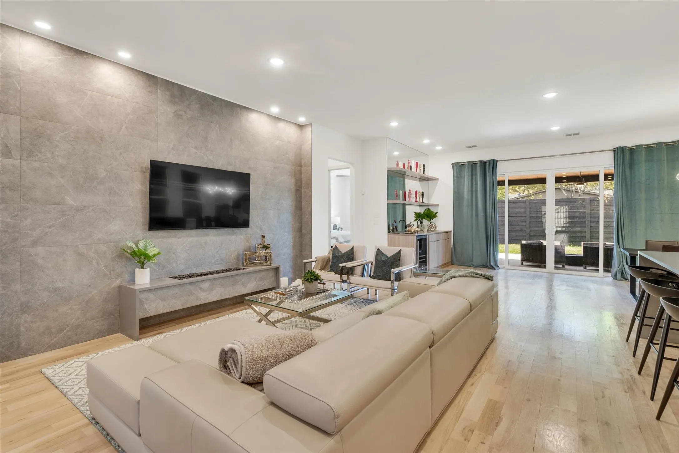 Modern open-concept living space featuring a wood-finish plank floor, custom concrete accent wall with integrated media console, and expansive seating area