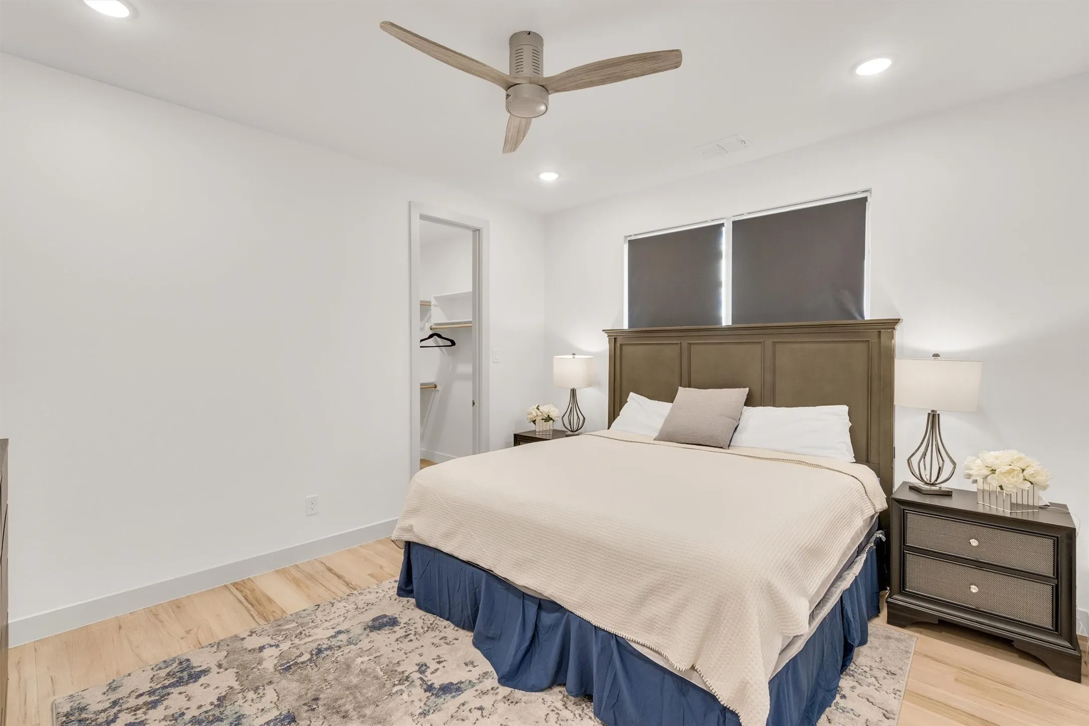 Primary bedroom featuring a wood-finish headboard with neutral bedding, hardwood flooring, recessed lighting, a ceiling fan with brushed metal finish, and a coordinating nightstand with integrated task lighting