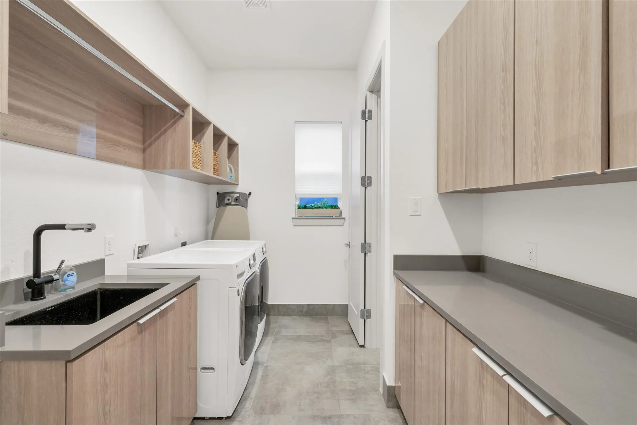 Light wood-finish cabinetry, gray countertops, and a black sink with a matte black faucet