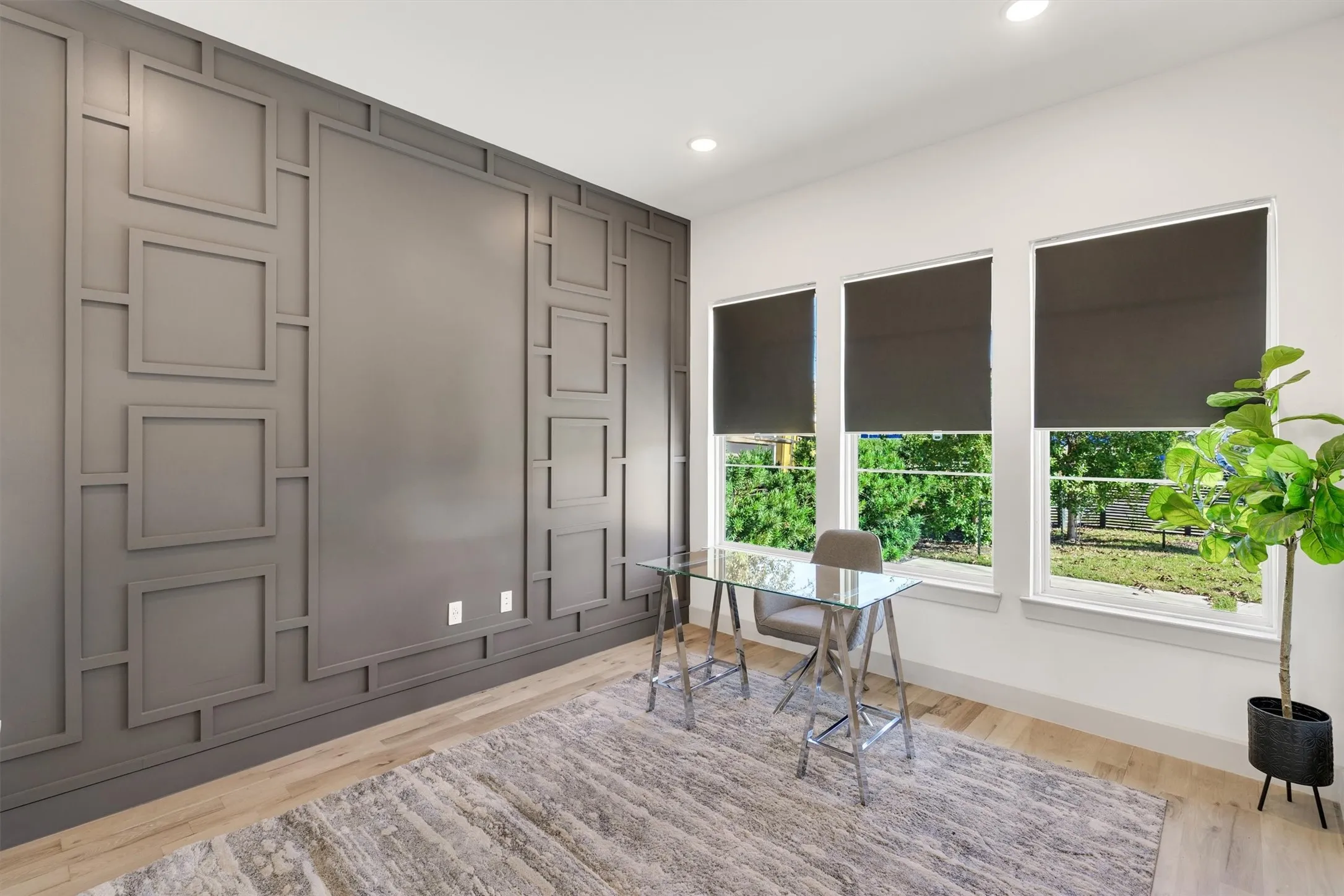 Accent wall featuring geometric panel molding, recessed ceiling lighting, natural wood-finish flooring, and multiple windows with roller shades