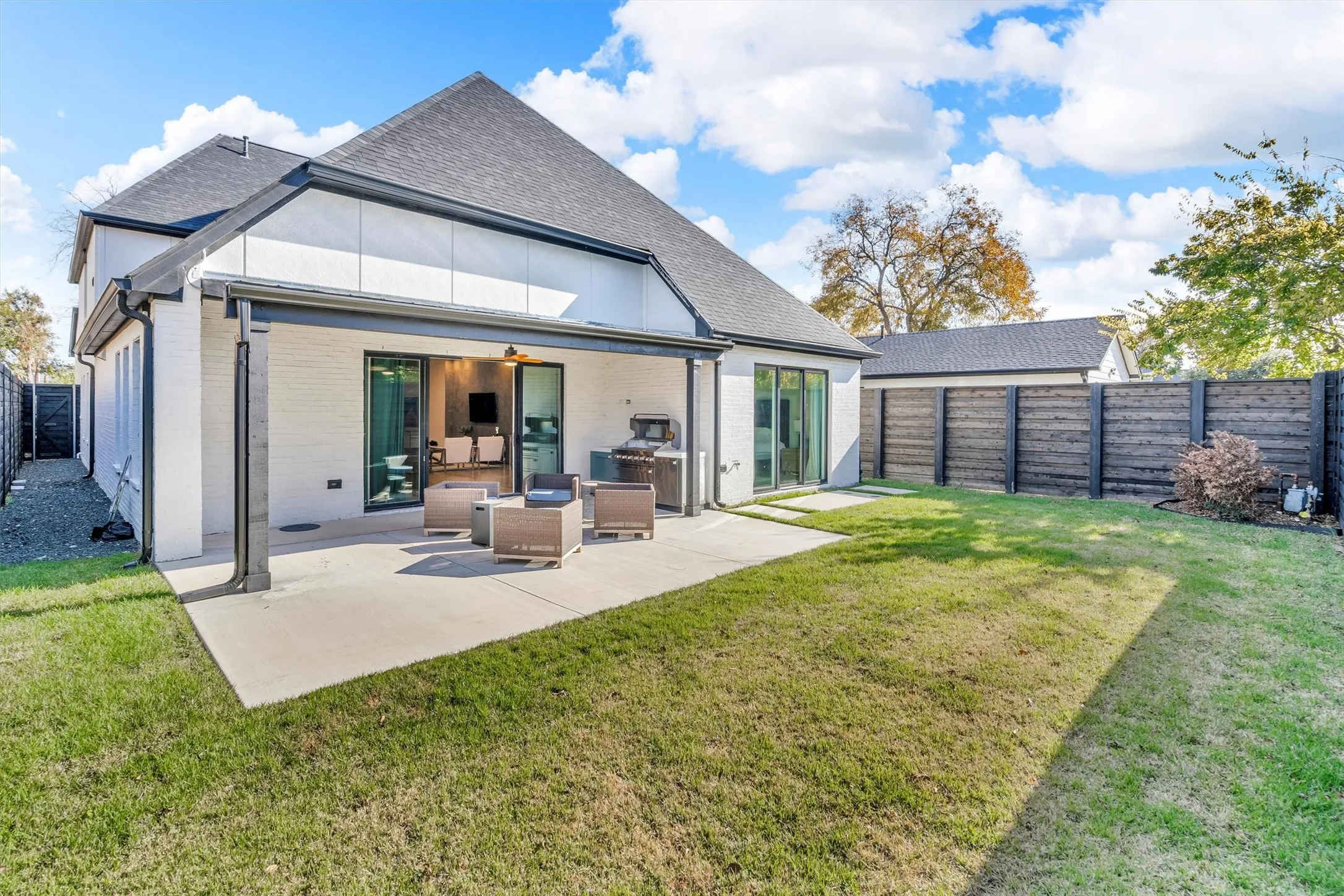 Expansive backyard with a covered patio, concrete paving, and a stained horizontal plank fence