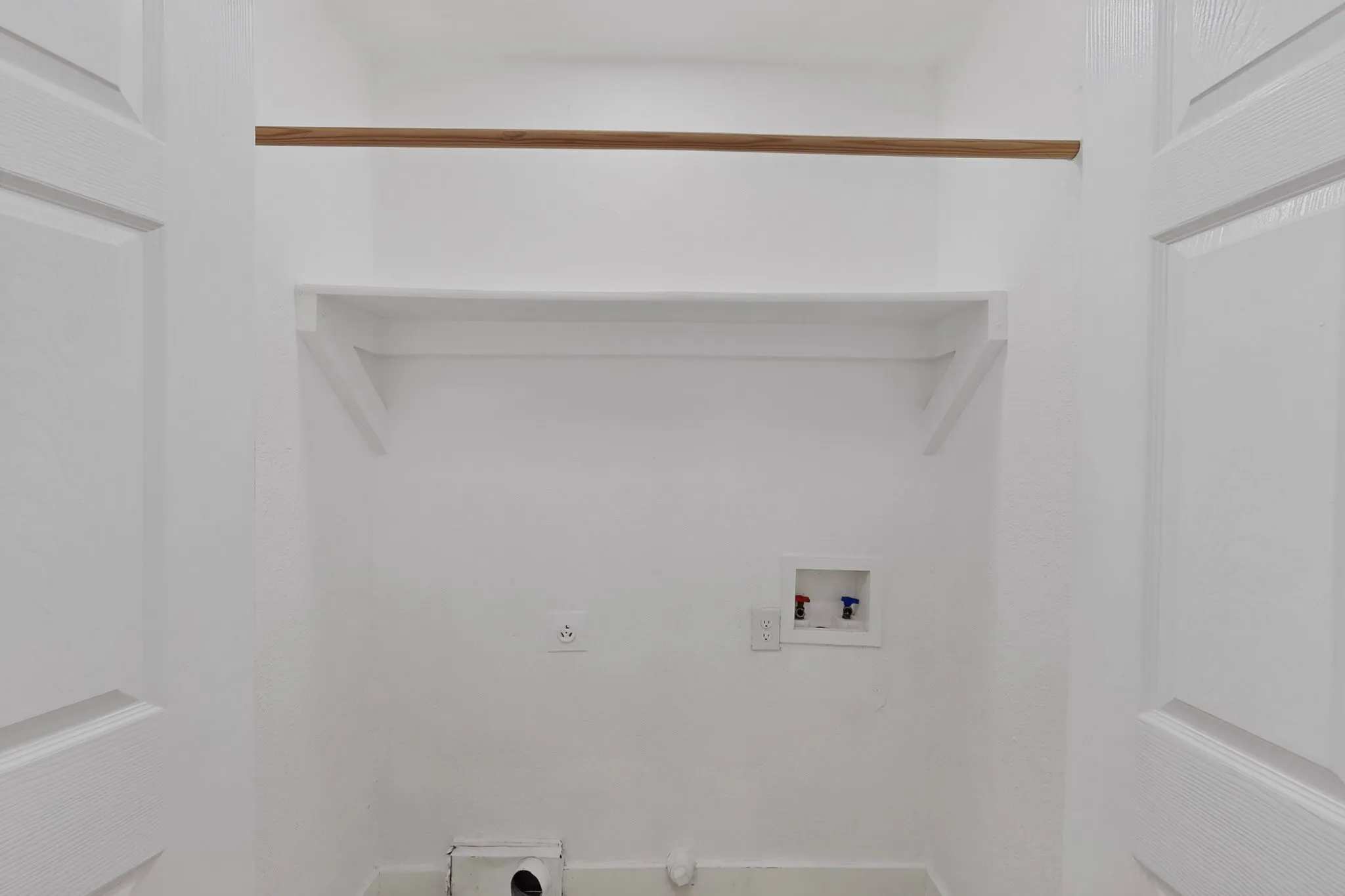 Dedicated laundry space featuring a built-in shelf, garment rod, and utility hookups