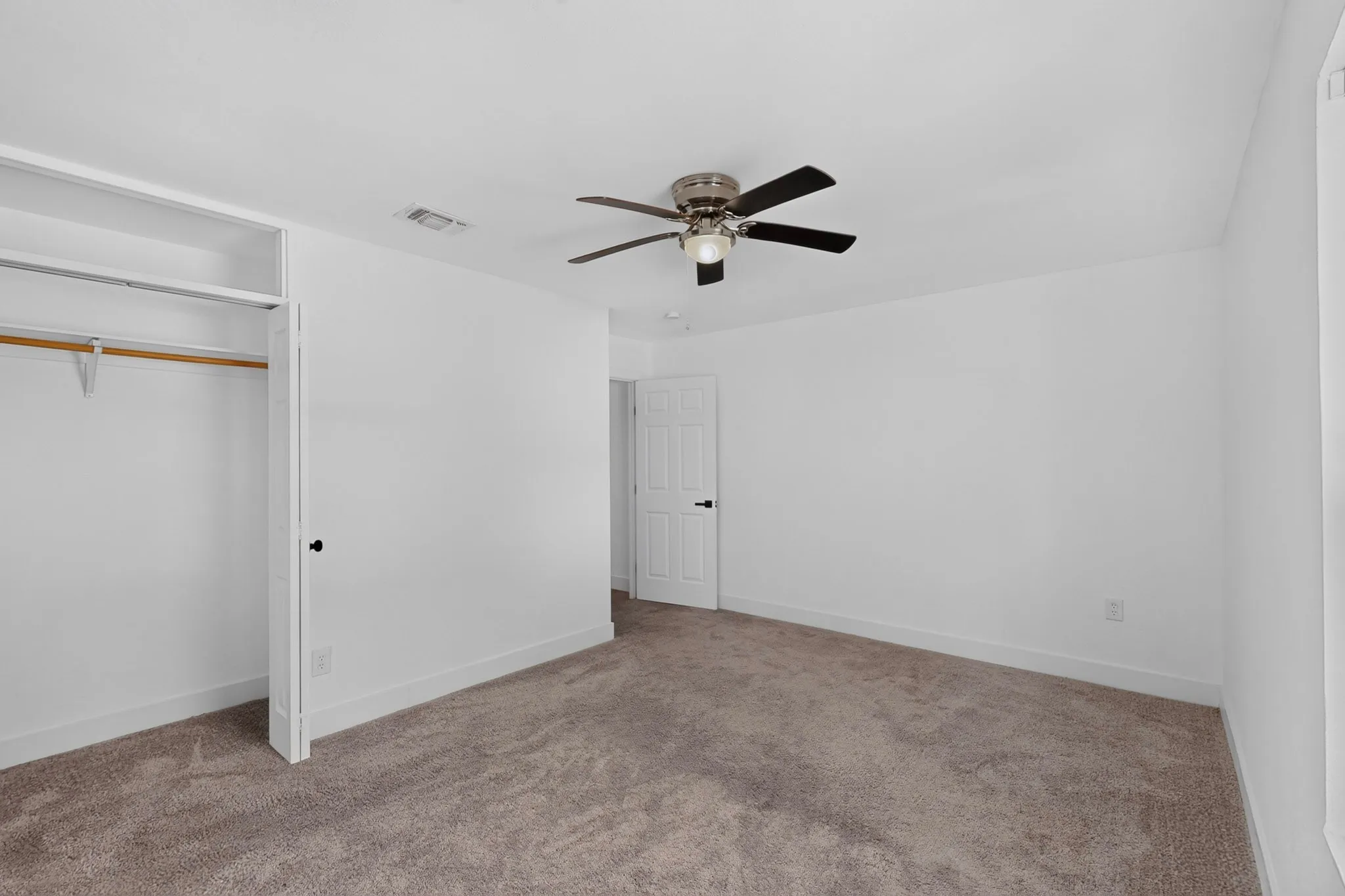 Carpeted room with a ceiling fan, white walls, and a built-in closet featuring a shelf and hanging rod