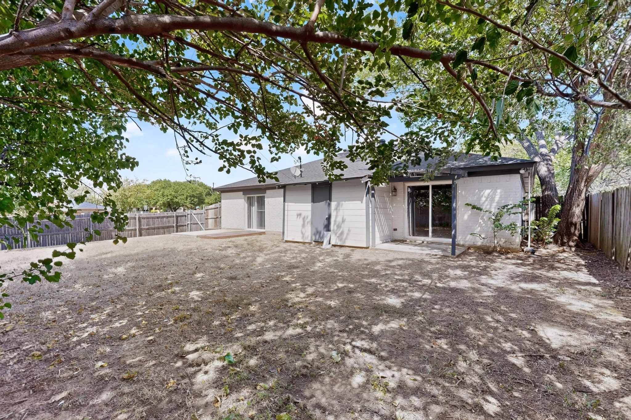 Expansive backyard with a wood privacy fence, concrete patio, and mature trees providing natural shade