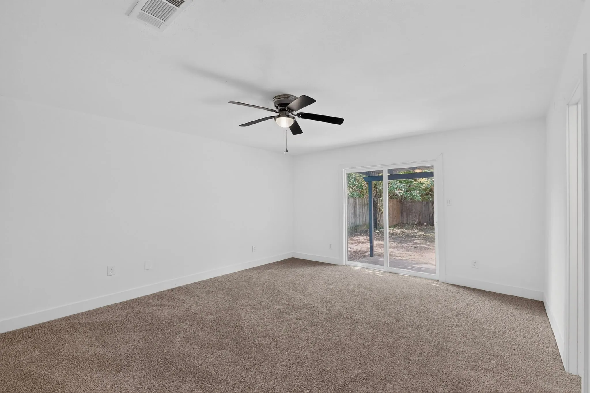 Spacious room featuring neutral carpet, white walls, a ceiling fan, and sliding glass doors to the exterior