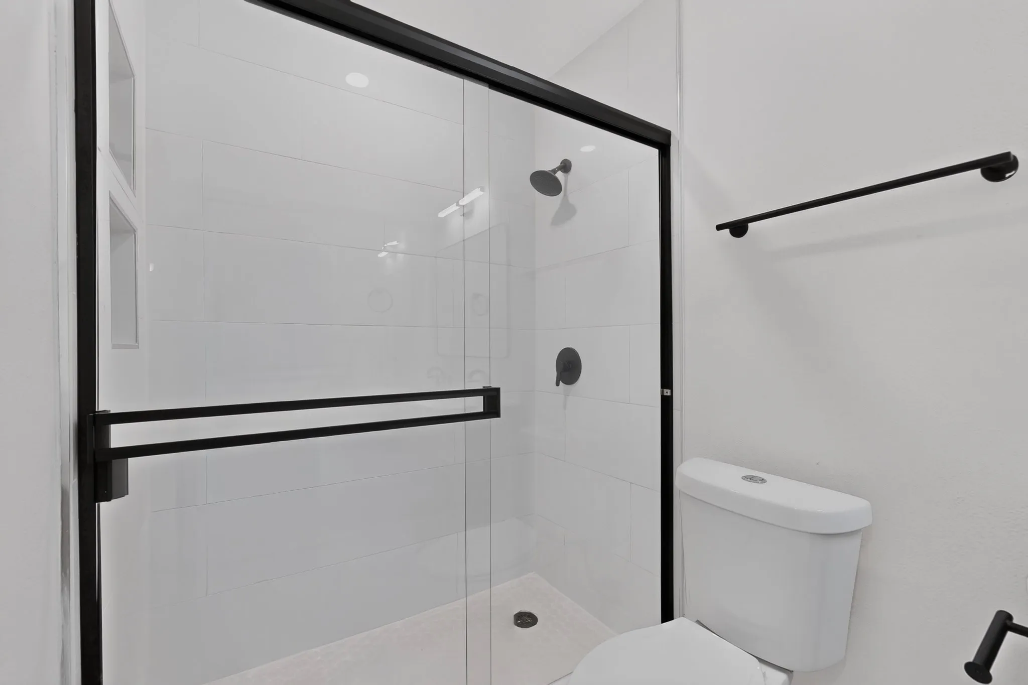 Glass-enclosed shower with matte black hardware, white subway tile surround, recessed shower niche, and a white​​‌​​​​‌​​‌‌​‌‌​​​‌‌​‌​‌​‌​​​‌​​ toilet