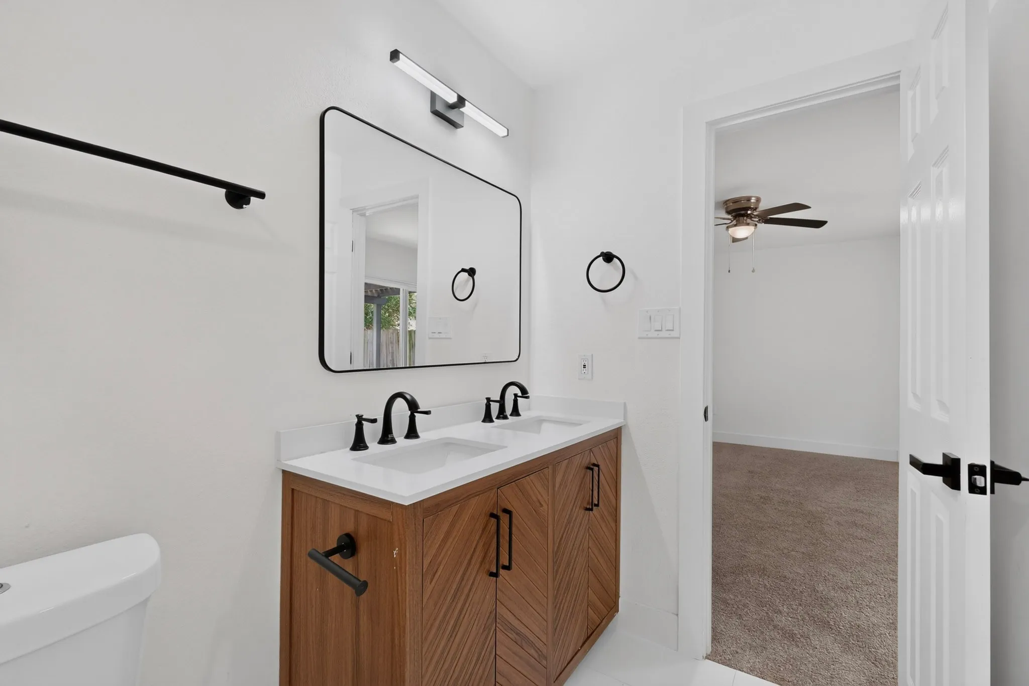 Modern primary bathroom featuring a wood-finish vanity with dual sinks, white quartz countertop, and matte black hardware