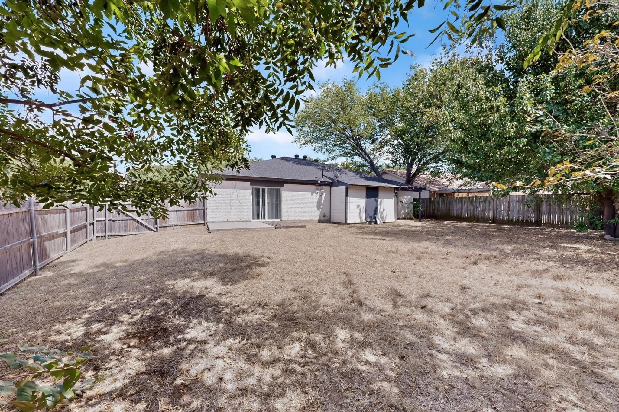 Spacious backyard featuring a full privacy fence, mature trees, and a concrete patio