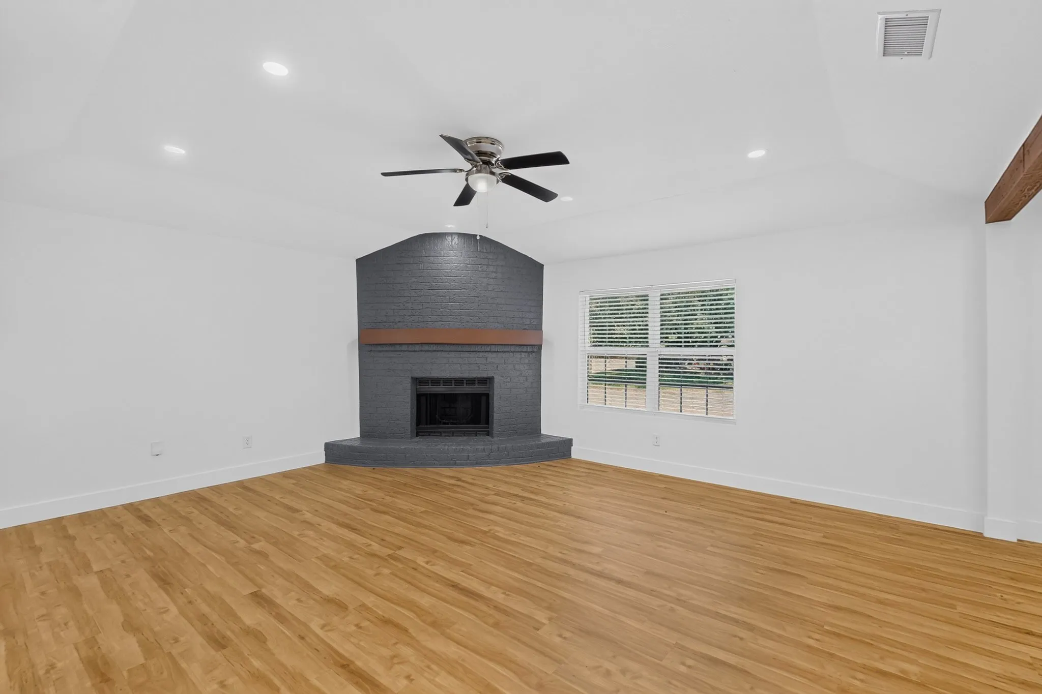 Spacious room showcasing warm wood-finish flooring, recessed ceiling lighting, and a ceiling fan