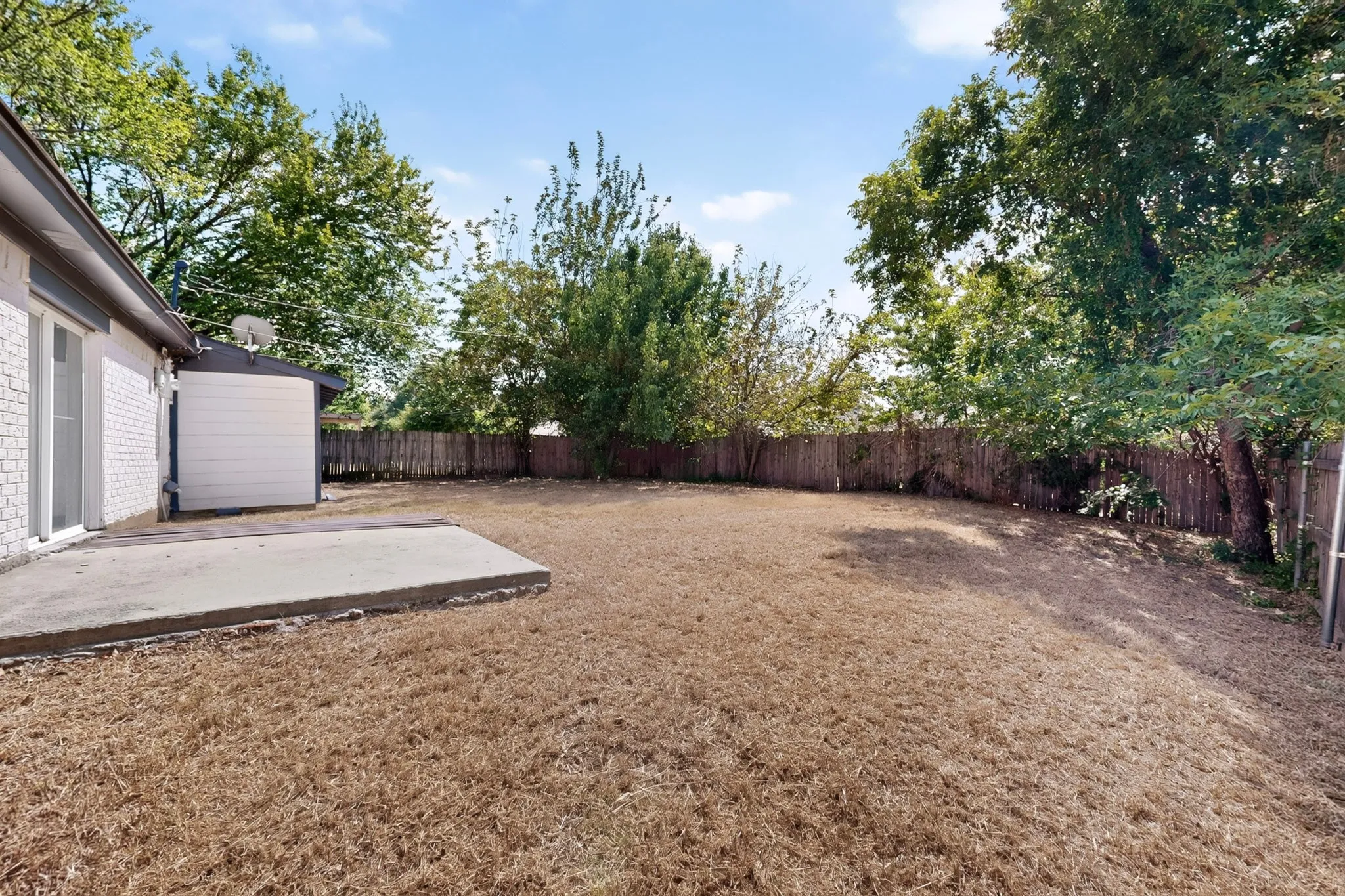 Expansive backyard featuring a concrete patio, white brick exterior, sliding glass door, and privacy fencing