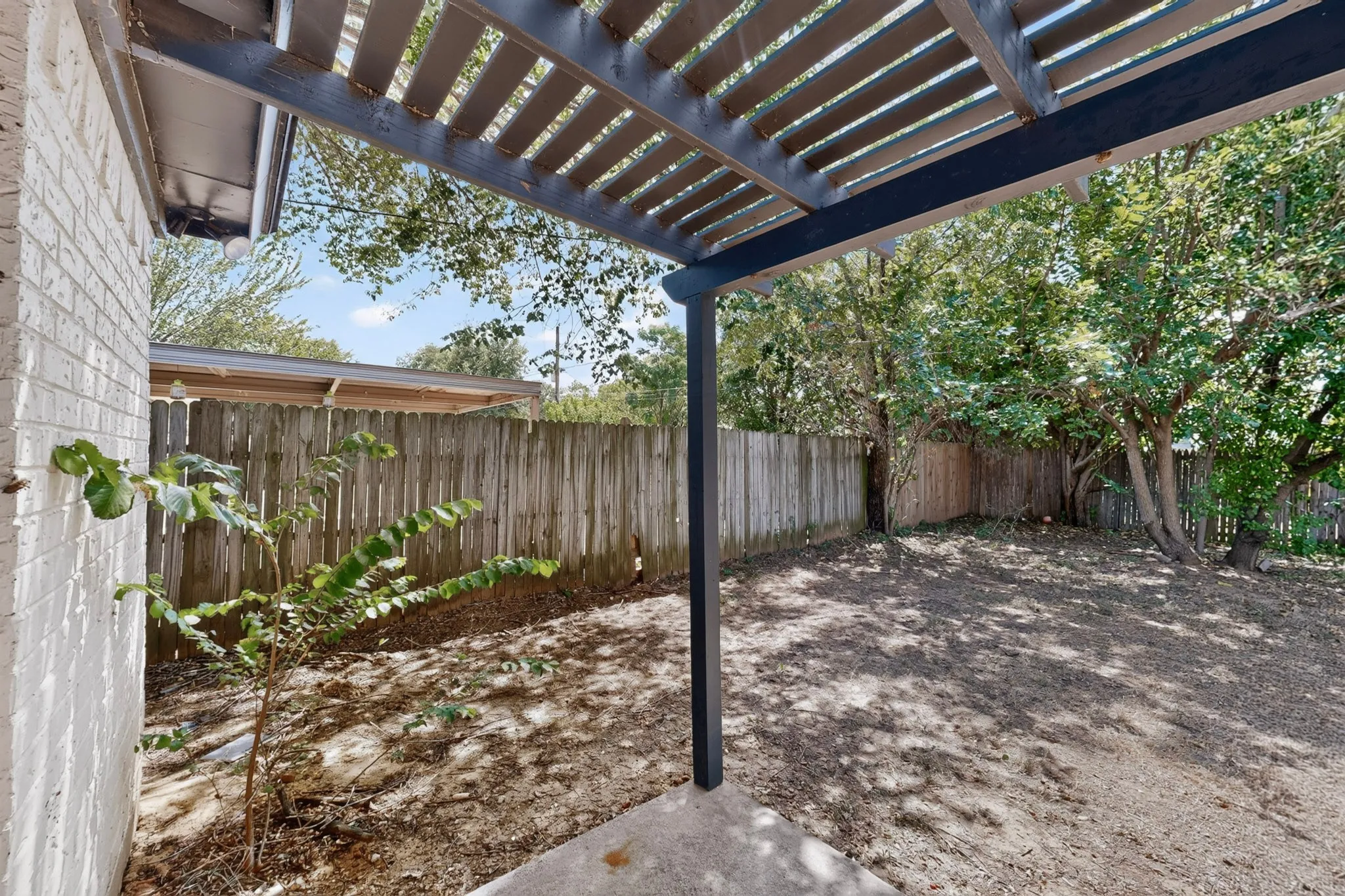 Spacious backyard oasis featuring a modern pergola with metal framing, mature landscaping with established trees, wooden privacy fencing, and ample ground space ideal for outdoor entertaining and recreation