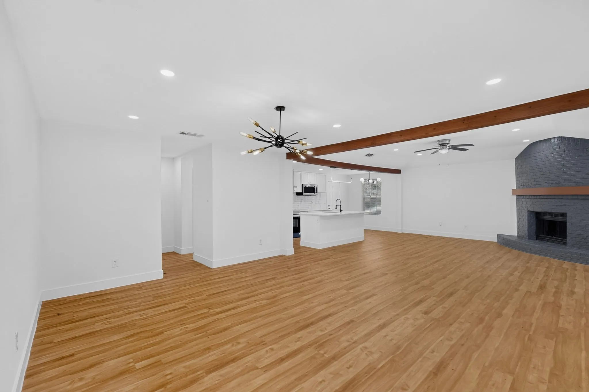 Open-concept living area showcasing wood-finish flooring, recessed ceiling lighting, and exposed wooden ceiling beams