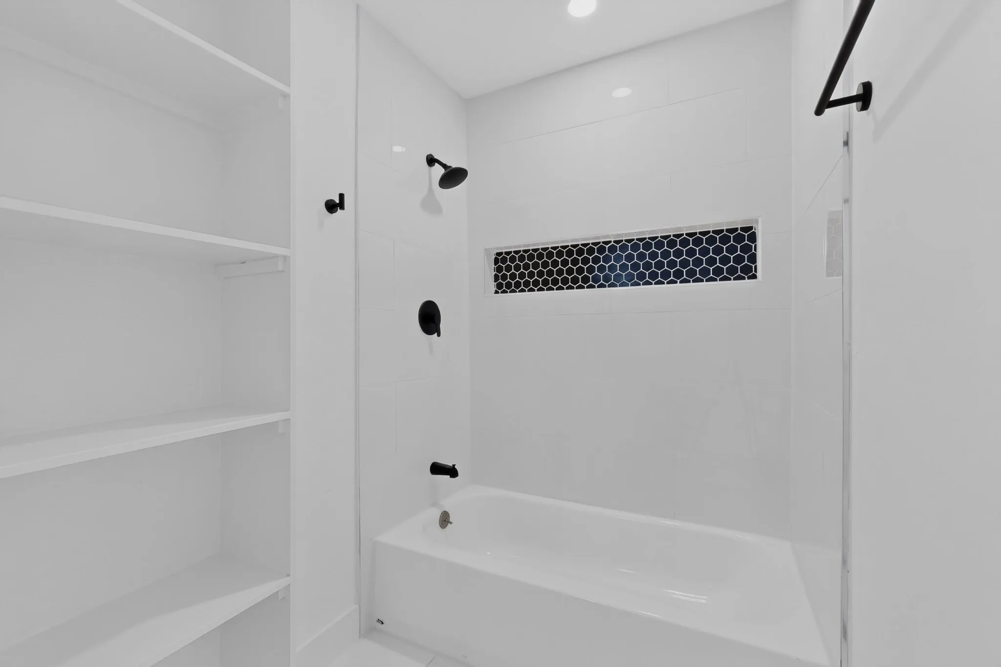 Built-in shelving, white subway tile surround, matte black fixtures, recessed light, and a black honeycomb tile accent