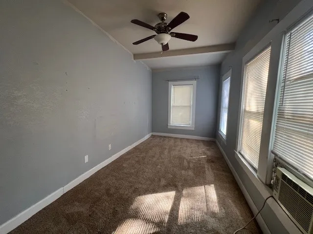 Carpeted spare room with ceiling fan and lofted ceiling with beams