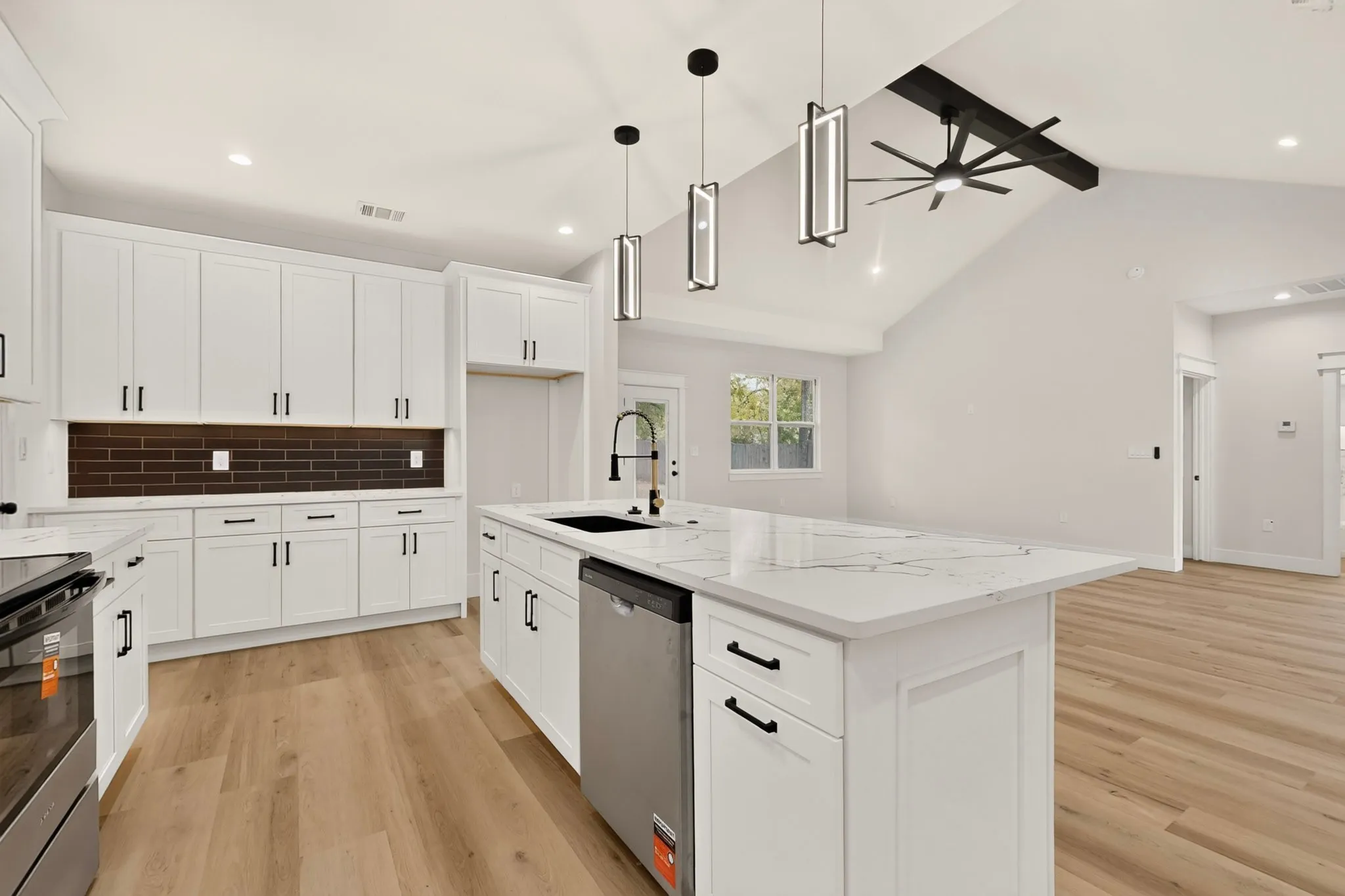 Kitchen featuring white shaker cabinetry, an island with a light-toned countertop, wood-finish flooring, a dark subway tile backsplash, and vaulted ceilings