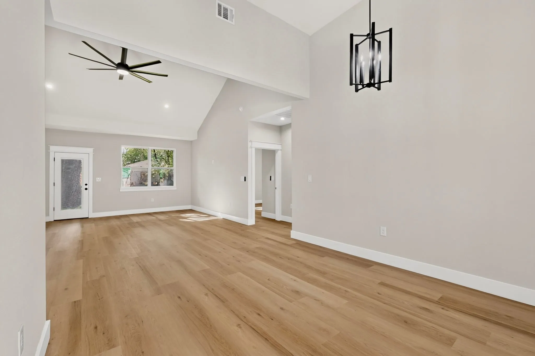 Vaulted ceilings, wood-finish flooring, modern ceiling fan, contemporary light fixture, and white trim throughout