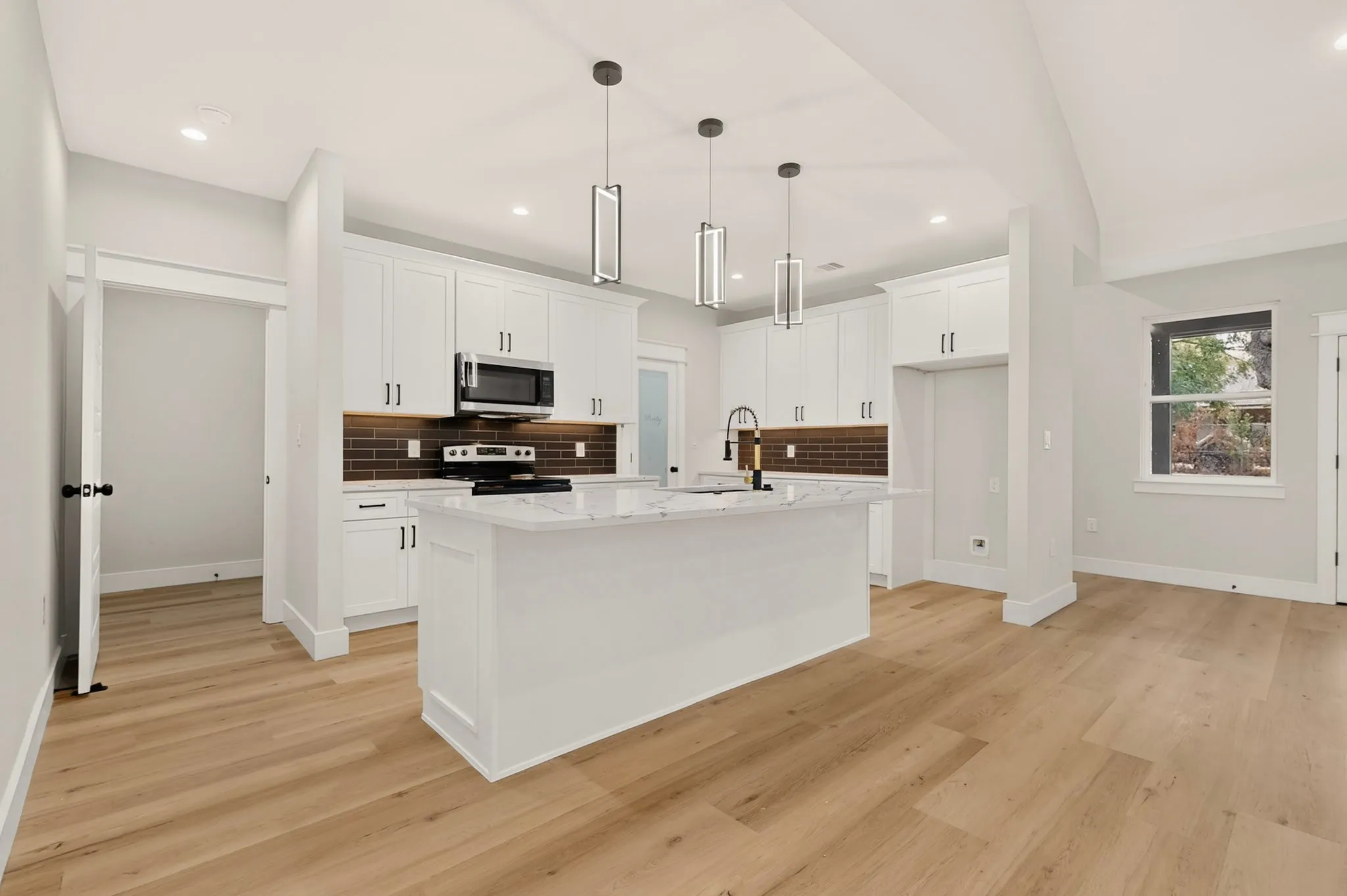 Open-concept kitchen with white cabinetry, a central island with a stone-finish countertop, and wood-finish flooring