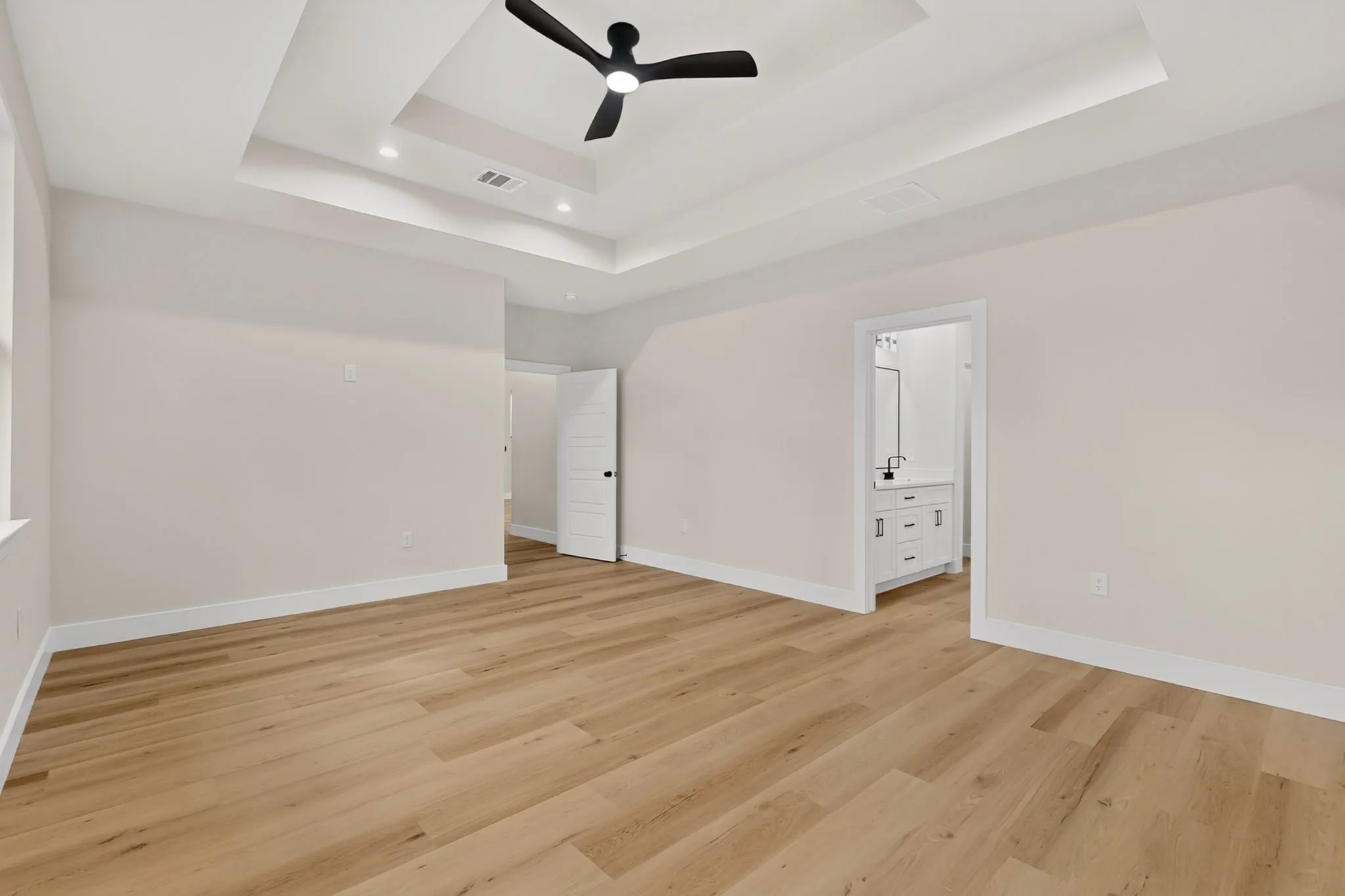 Recessed ceiling with a black ceiling fan, wood-finish flooring, and white interior doors