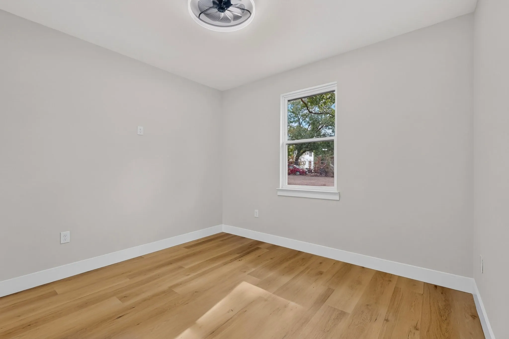 Wood-finish flooring, white trim, single window, and a ceiling-mounted light fixture