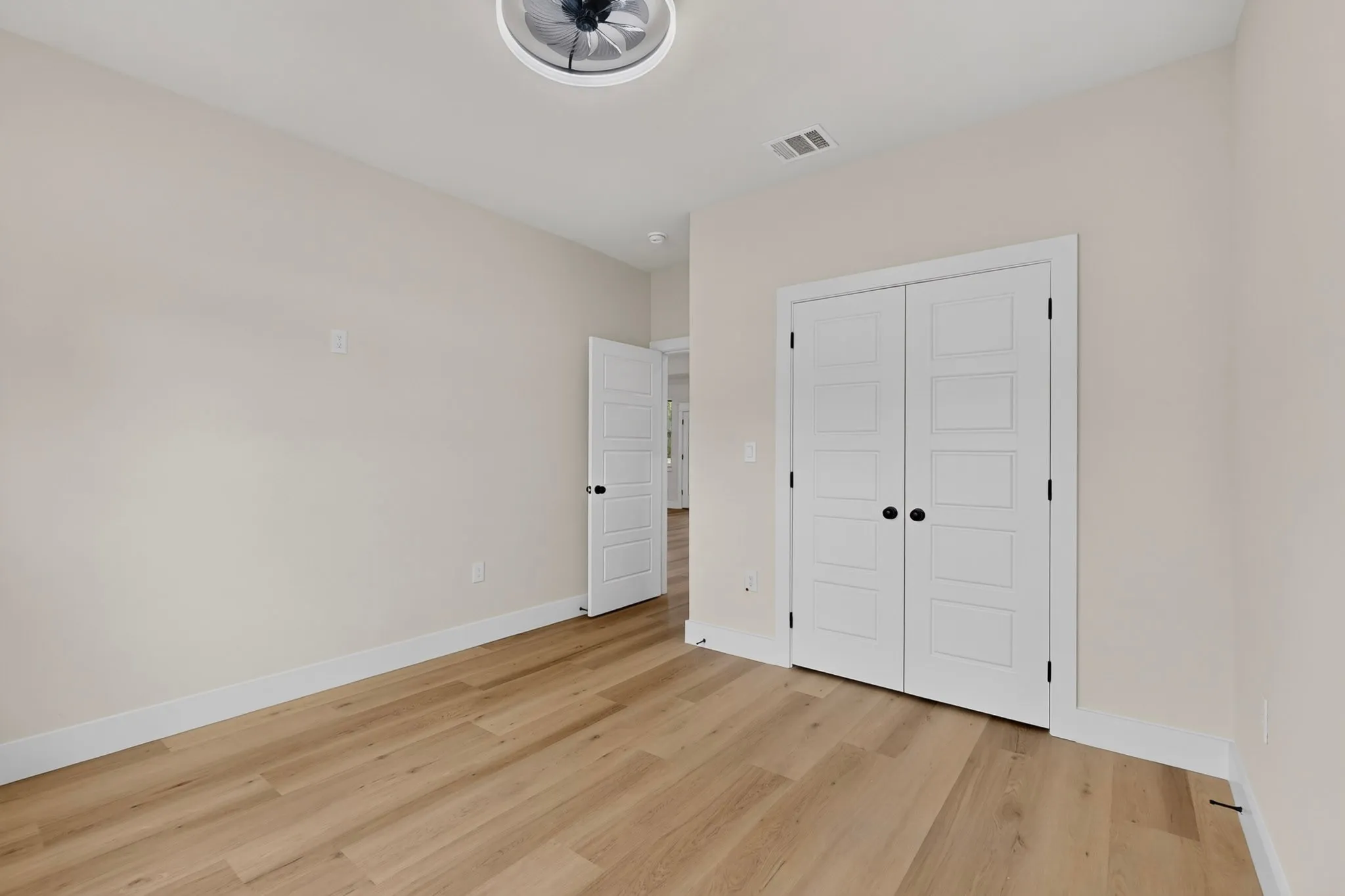 Wood-finish flooring throughout, bright white trim, and a modern ceiling fan with integrated lighting