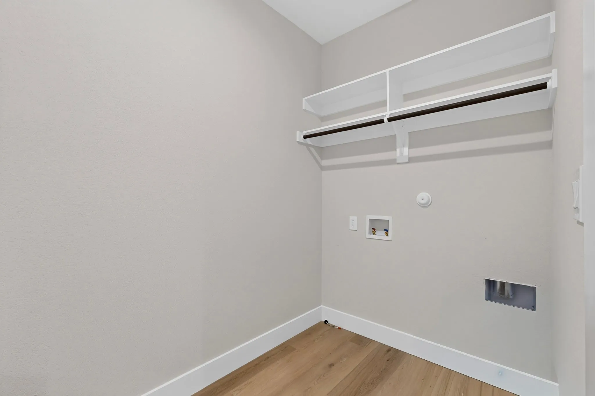 Dedicated laundry area featuring wood-finish flooring, white trim, and built-in shelving with hanging rods