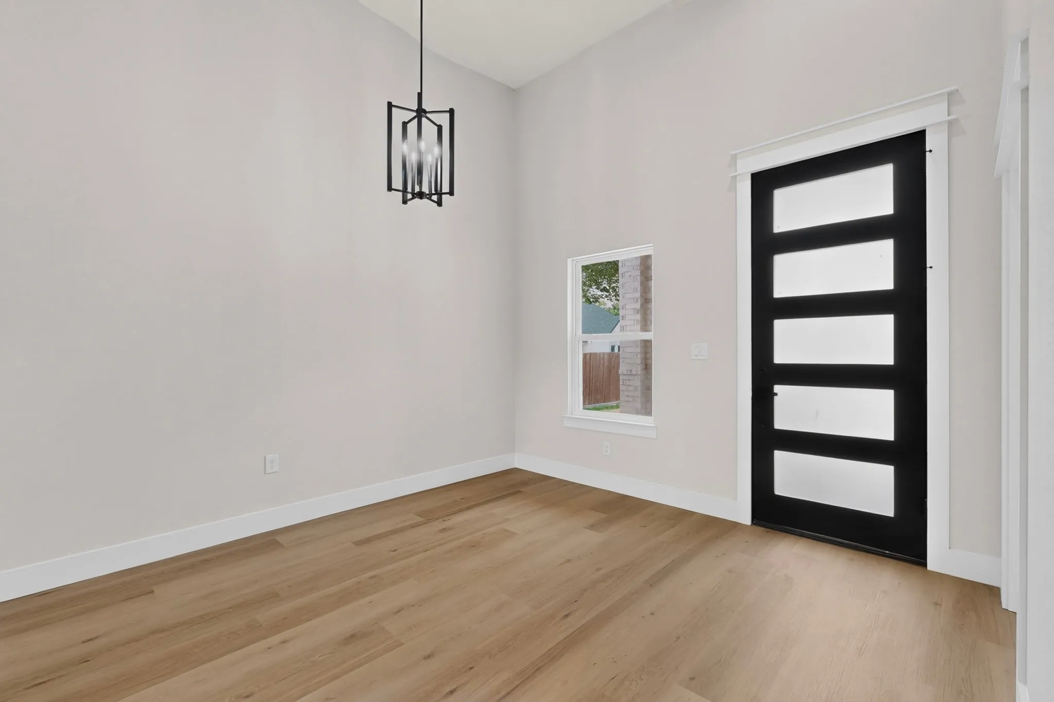 Wood-finish flooring, high vaulted ceiling, contemporary black light fixture, white trim, and a modern black door with translucent panels
