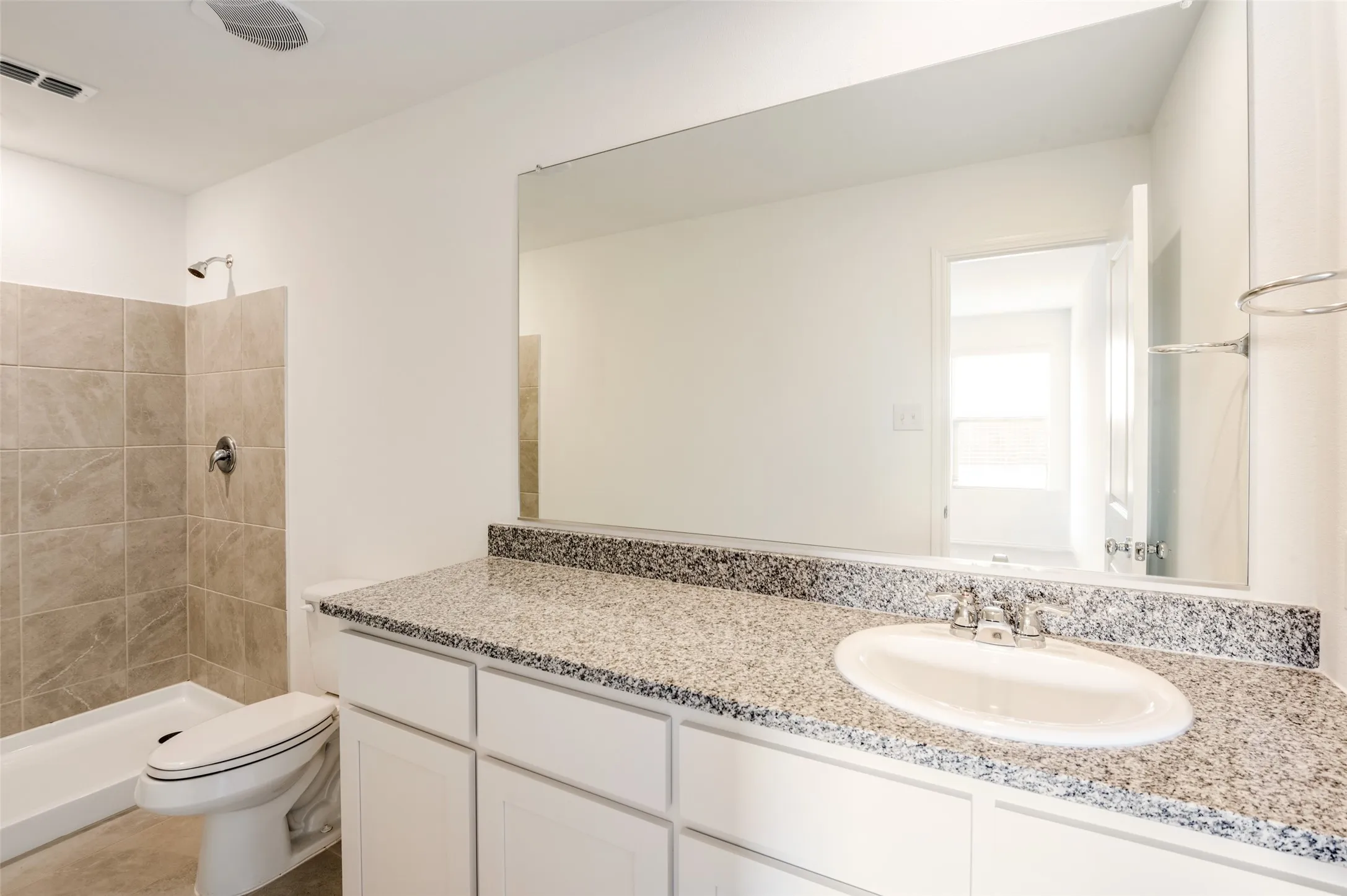 White vanity with an integrated sink, granite countertop, frameless mirror, and a tiled shower with a shower pan