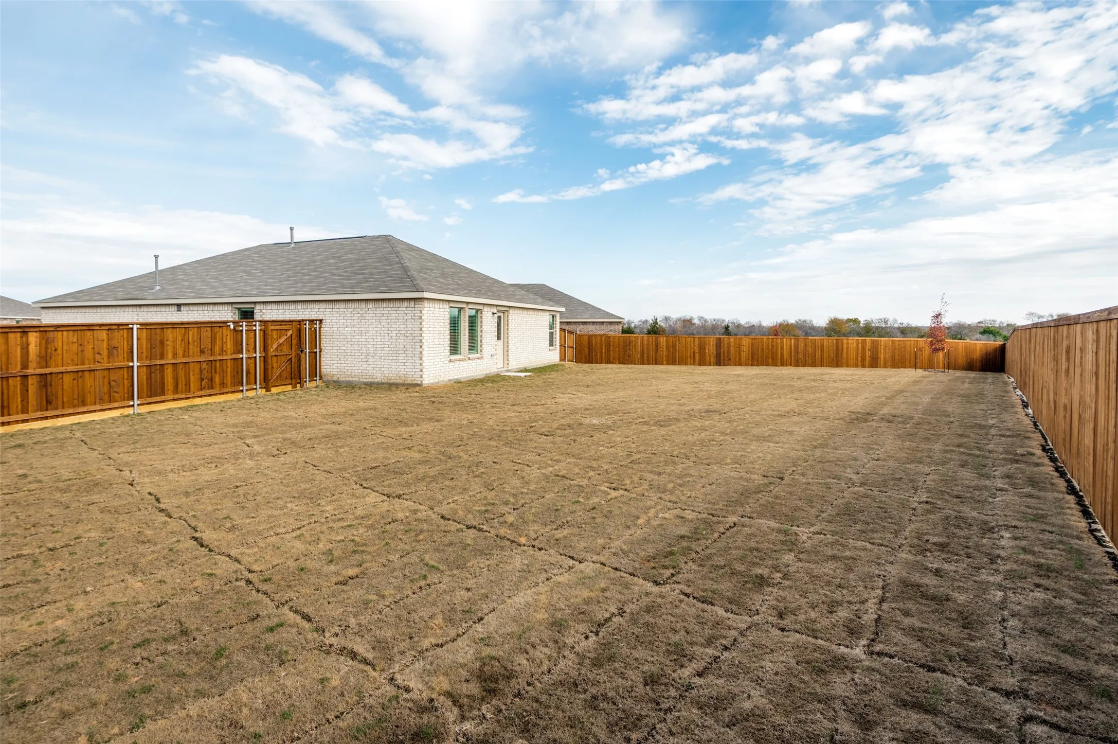 Expansive backyard featuring a natural grass area, wood privacy fencing, and a white brick exterior