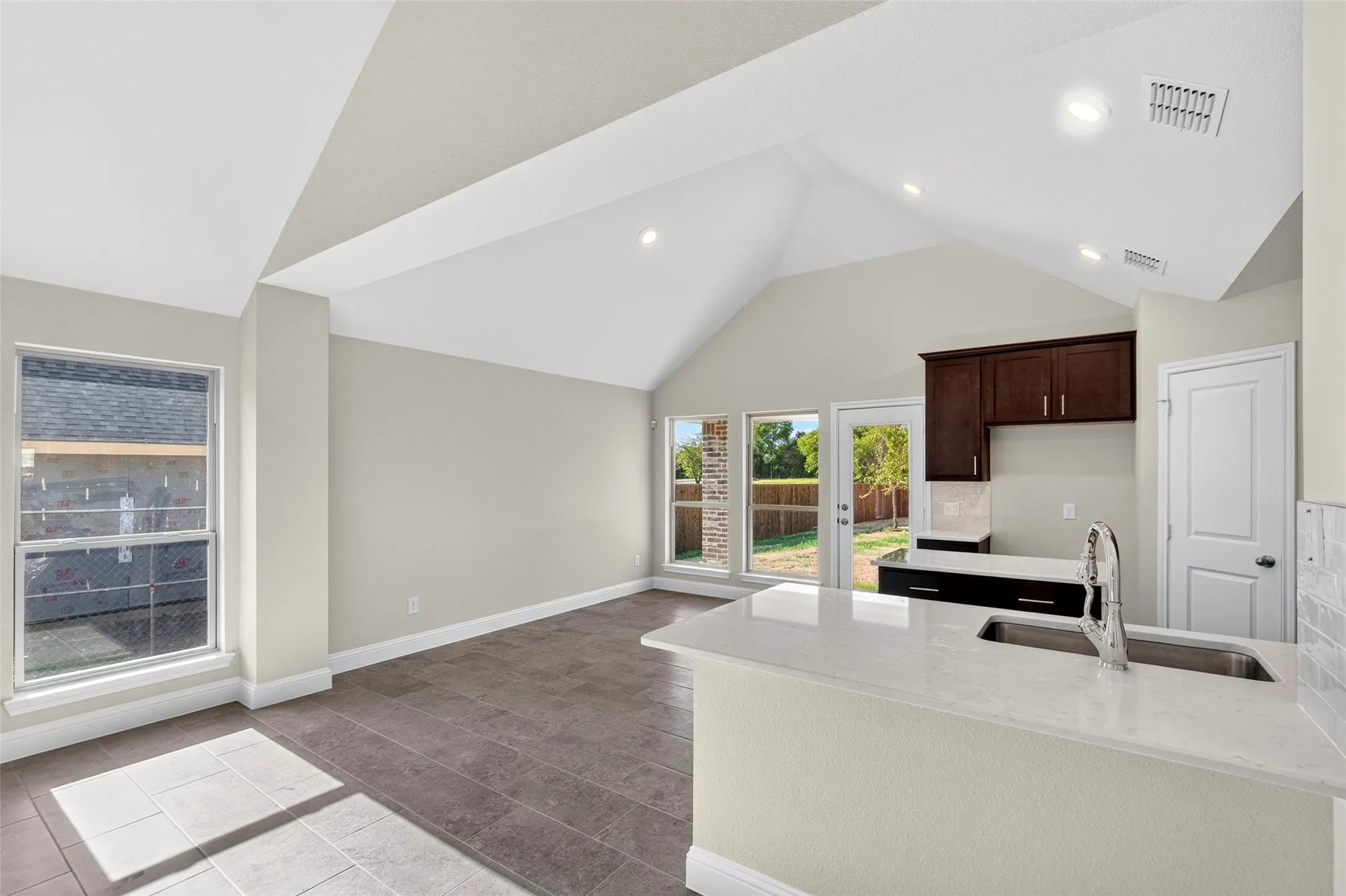 Vaulted ceiling, recessed lighting, tile flooring, kitchen island with sink, and dark wood cabinetry