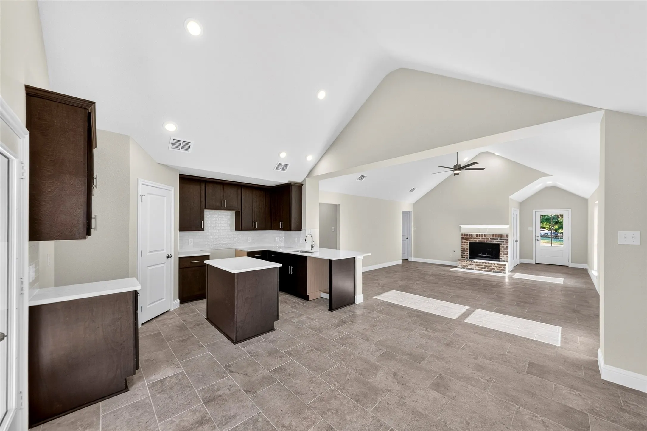 Spacious interior featuring a vaulted ceiling, recessed lighting, tile flooring, a fireplace with a brick surround, and dark wood-finish cabinetry