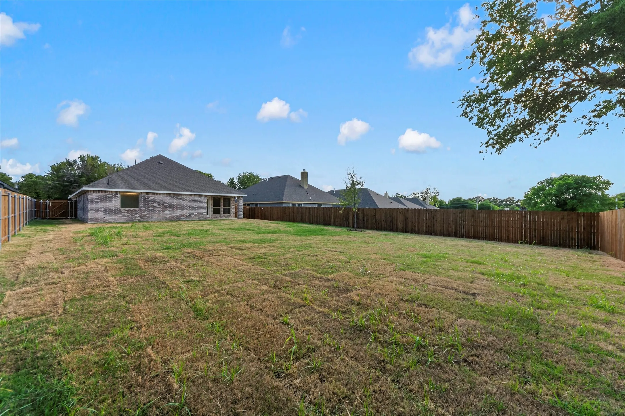 Expansive backyard with a wood privacy fence, featuring a brick exterior and a gabled roofline