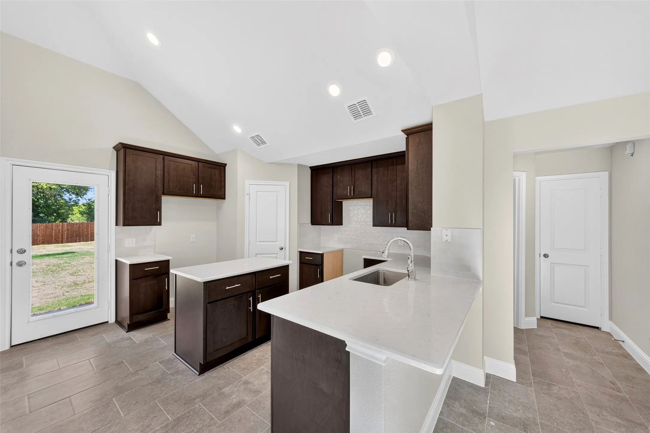 Kitchen featuring vaulted ceilings, recessed lighting, wood-finish cabinetry, light-toned countertops, and a stainless steel sink with a gooseneck faucet