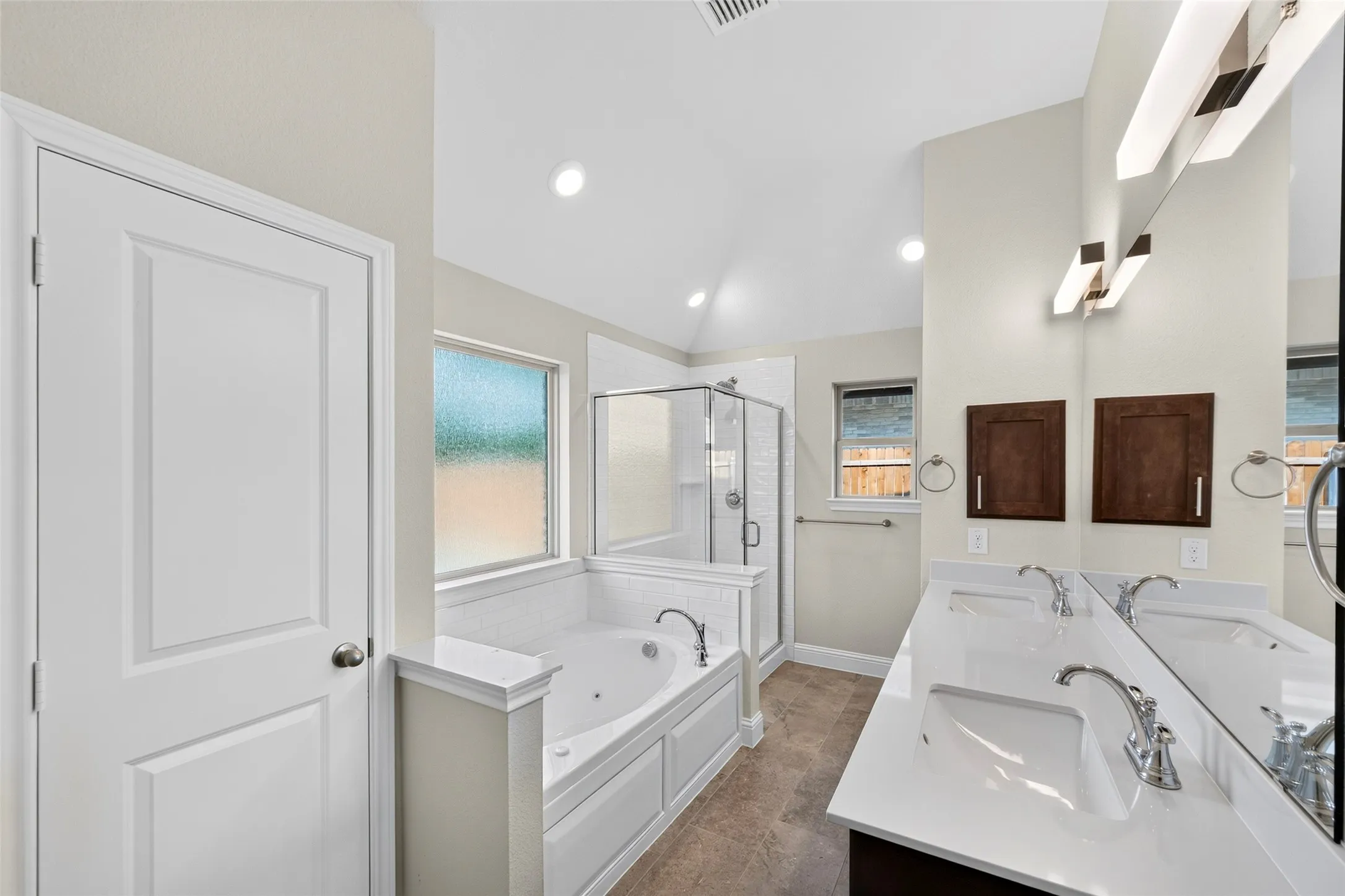 Dual vanity with integrated sinks, jetted soaking tub, separate glass-enclosed shower, wood-finish flooring, and recessed lighting