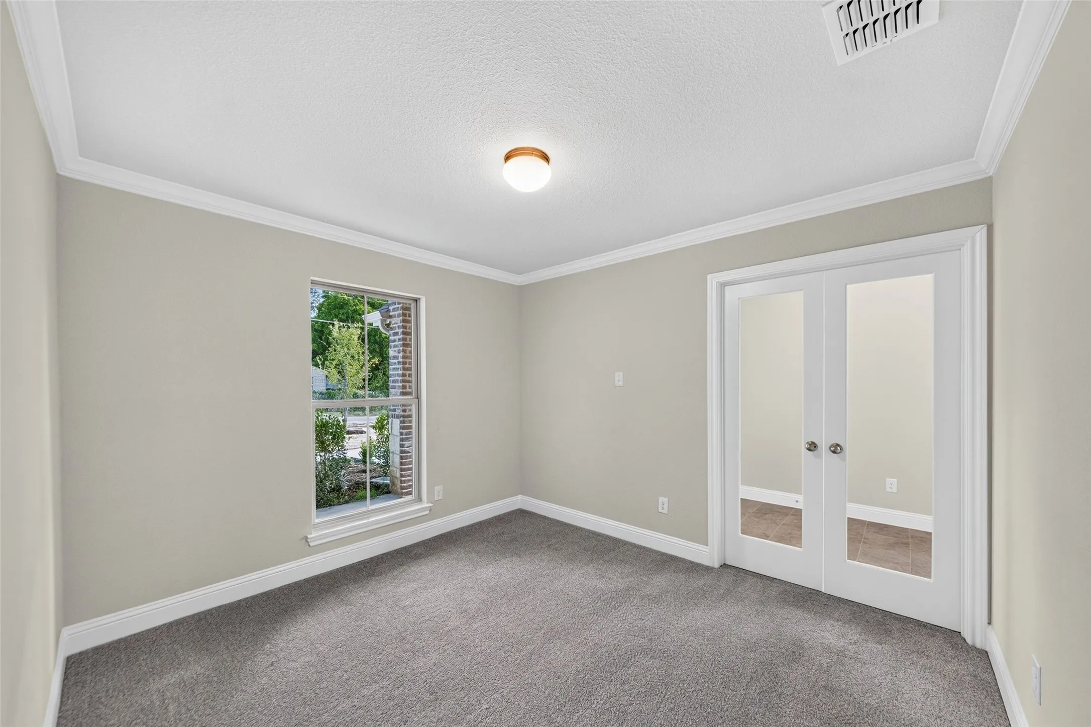 Neutral wall color, gray carpet, crown molding, double French doors, and a window with a brick exterior visible