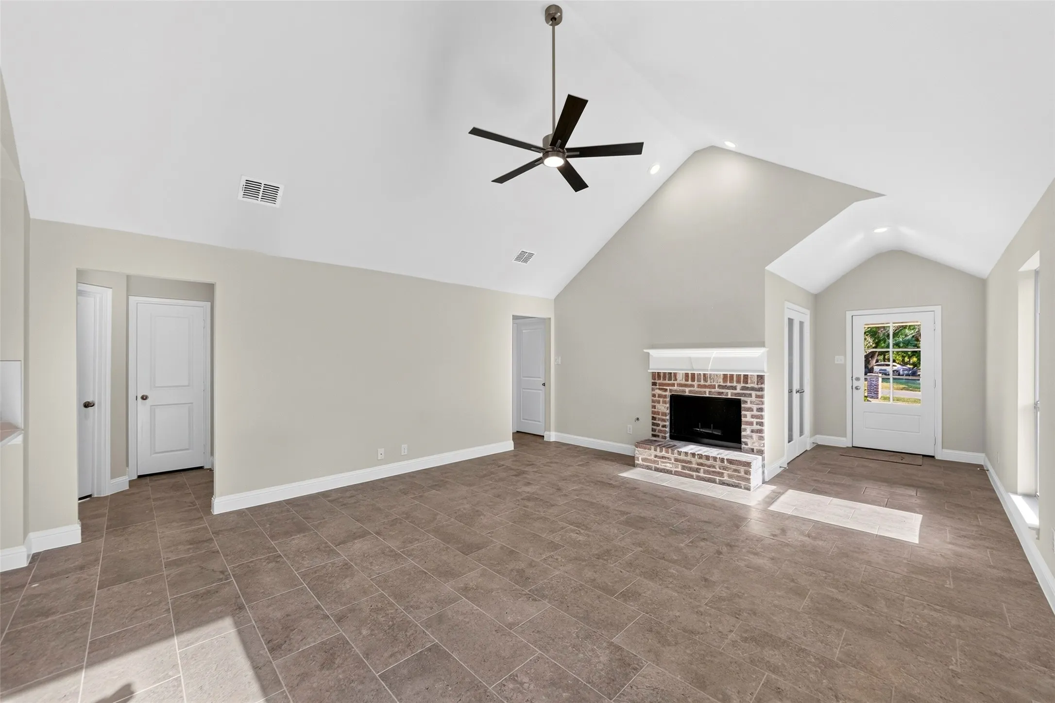 Vaulted ceilings with a ceiling fan, brick fireplace, tiled flooring, and a glass-paneled entry door