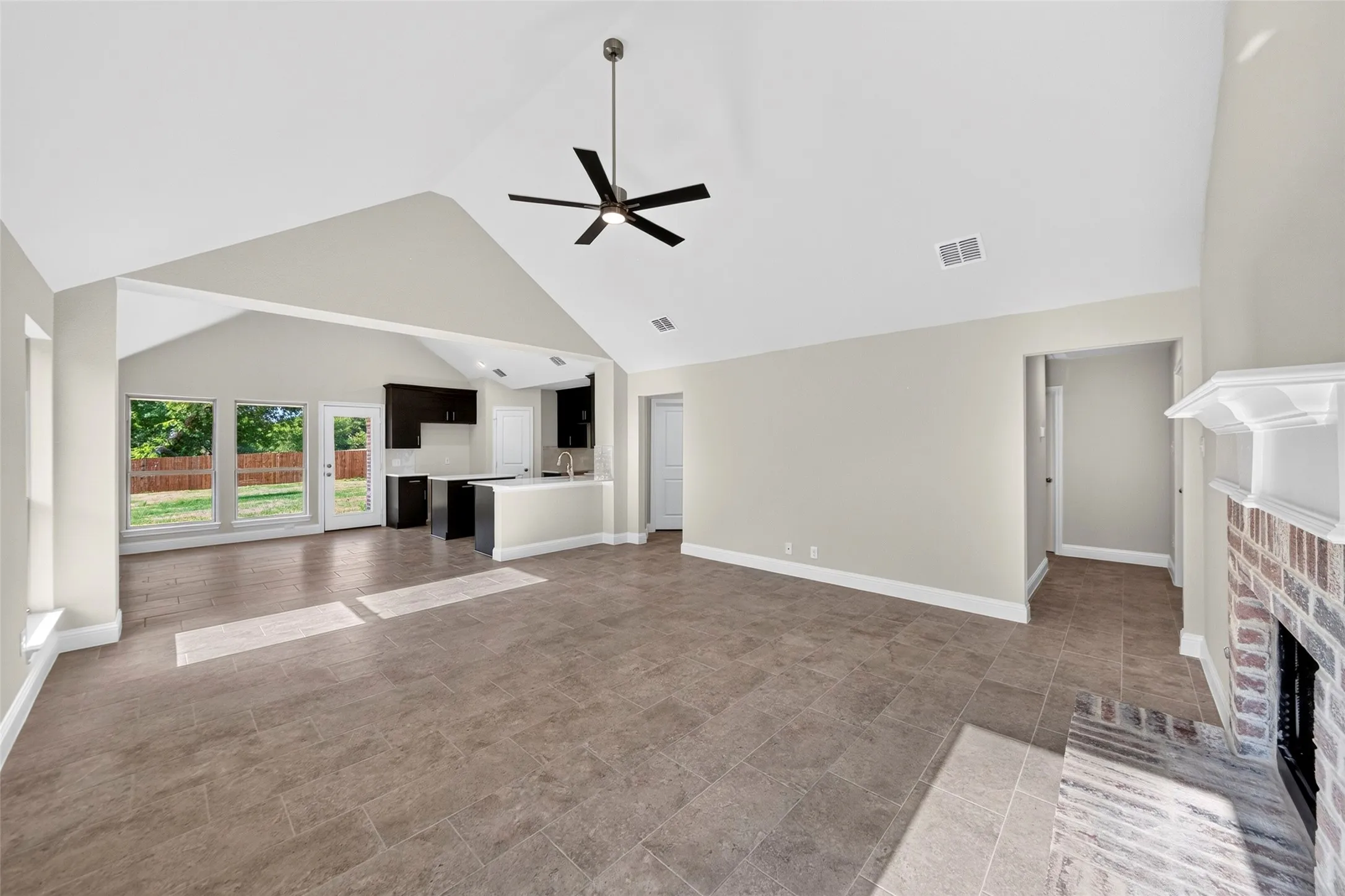 Vaulted ceiling with a ceiling fan, brick fireplace, tile flooring, and a kitchen island with a built-in sink