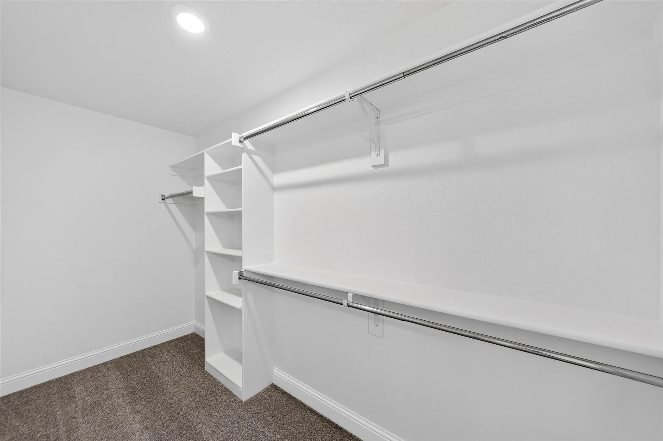 Recessed lighting illuminates extensive white shelving and chrome hanging rods