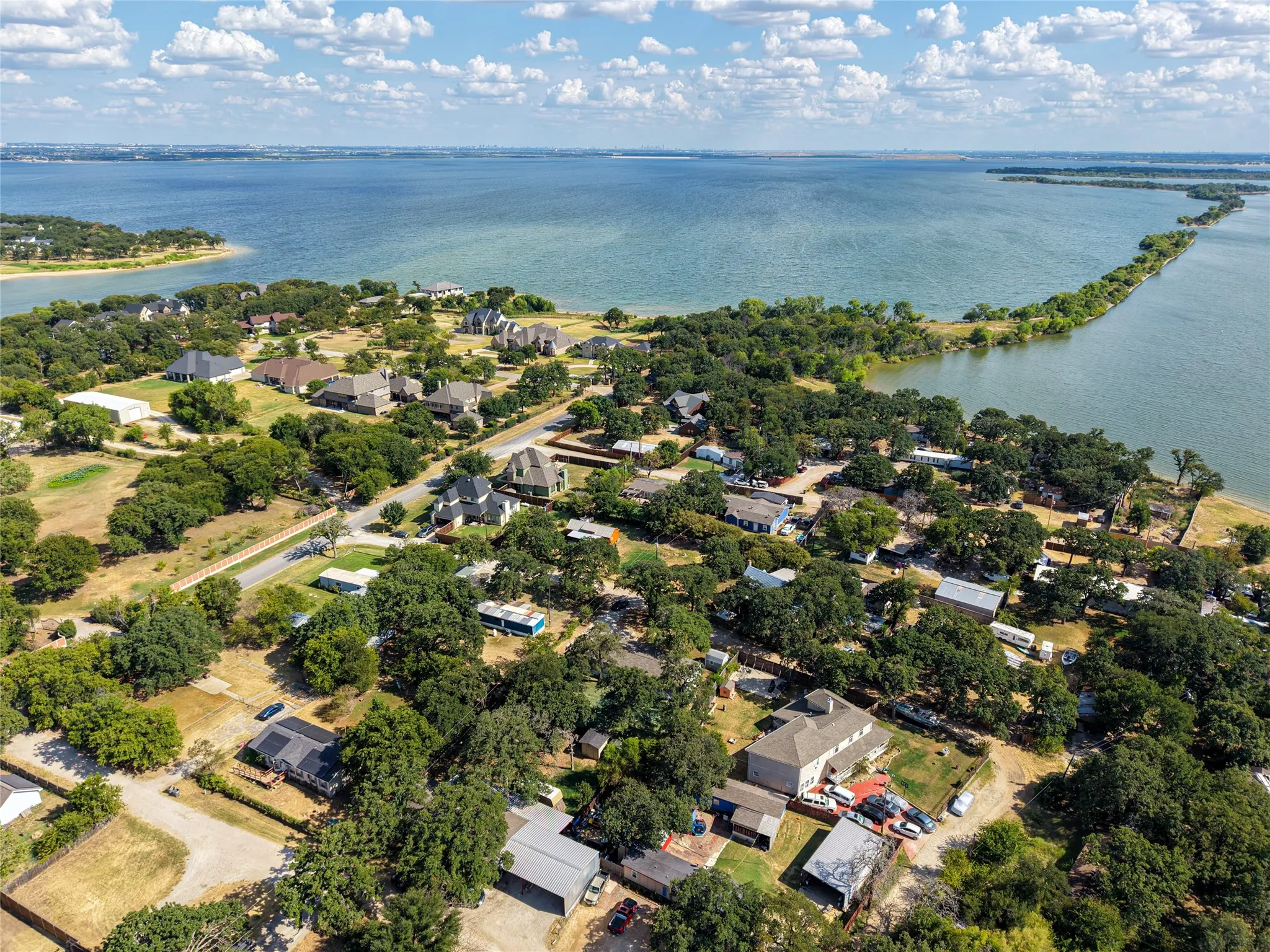 Expansive waterfront setting featuring a large body of water, lush green trees, and multiple residential structures