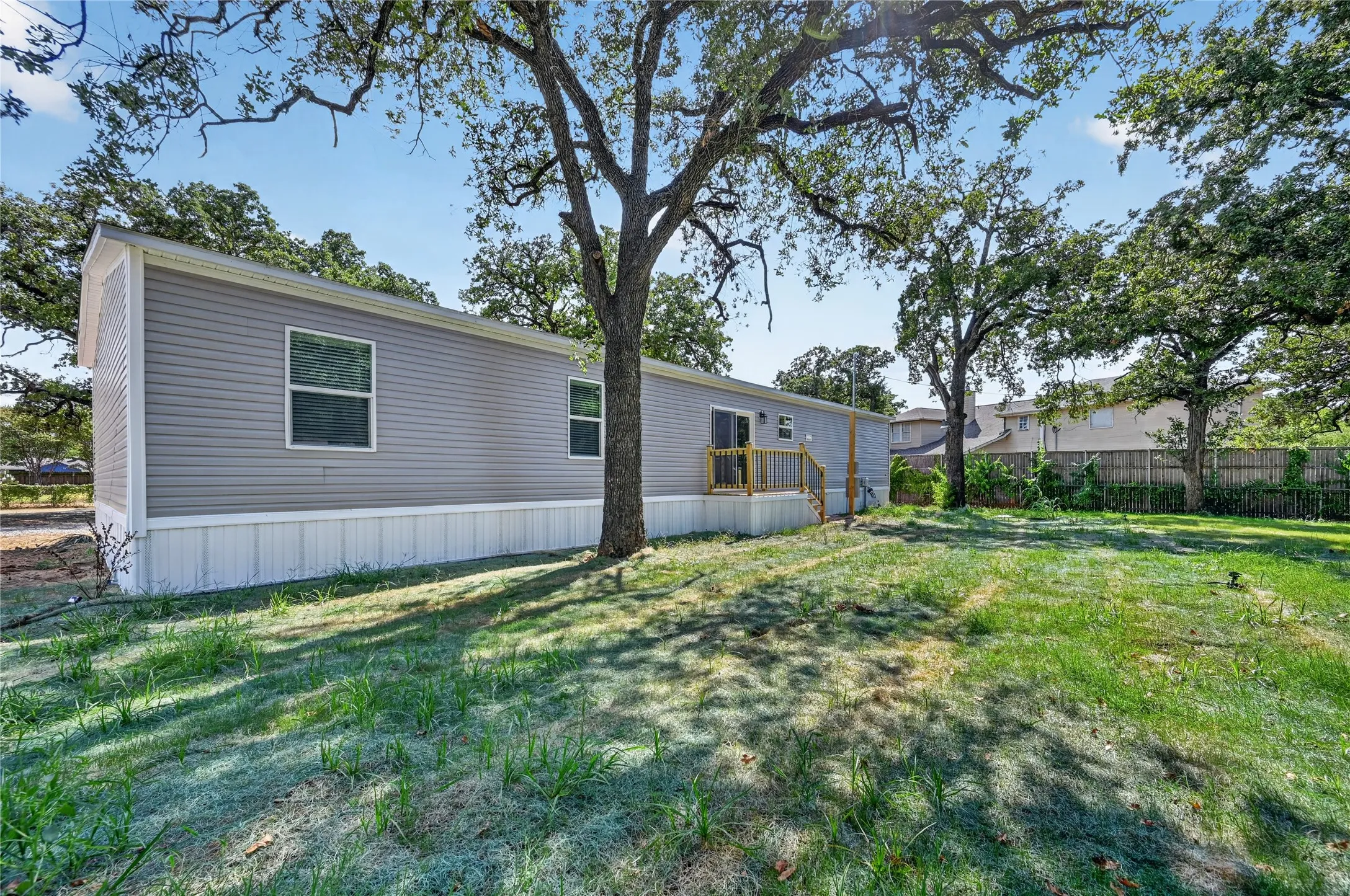 Siding exterior with multiple windows, wooden deck, and a spacious lawn