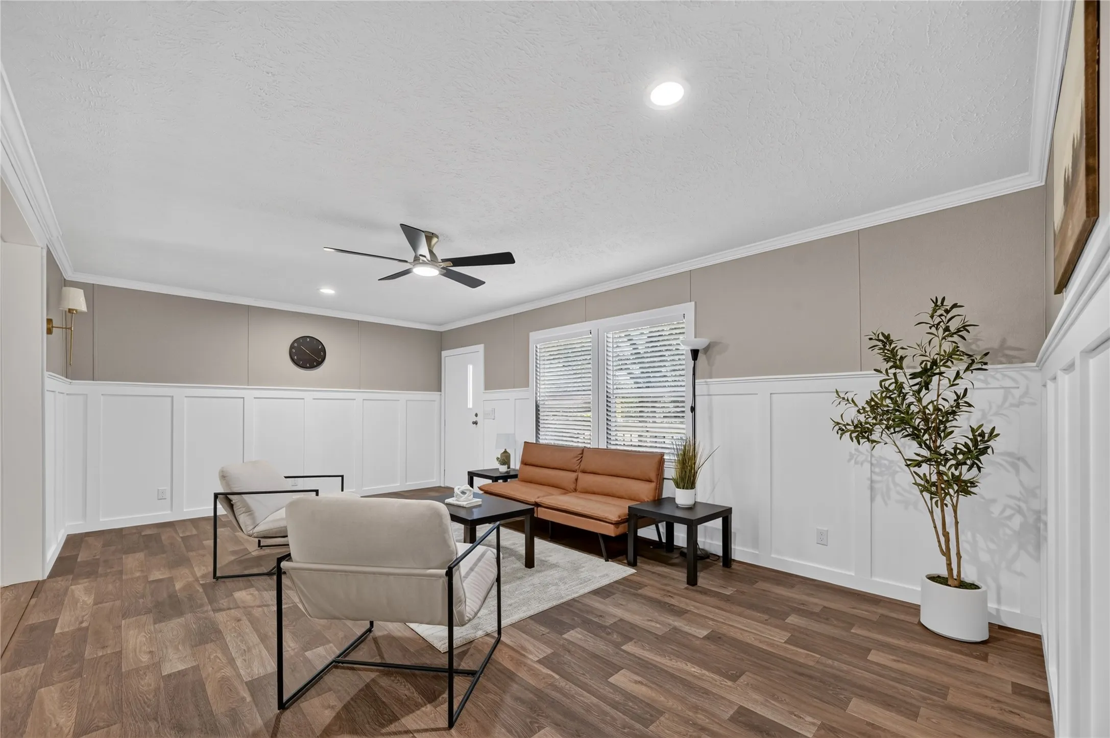 Spacious room featuring wood-finish flooring, white wainscoting, and a ceiling fan