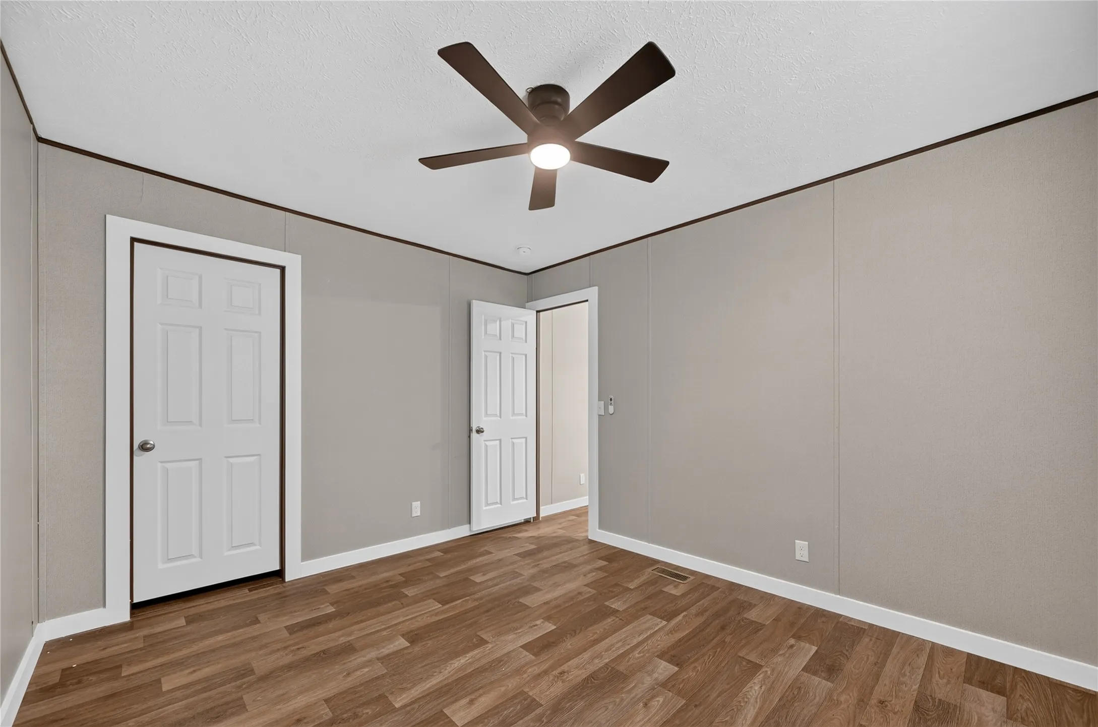 Wood-finish flooring, ceiling fan with integrated lighting, two panel doors, and neutral wall tones