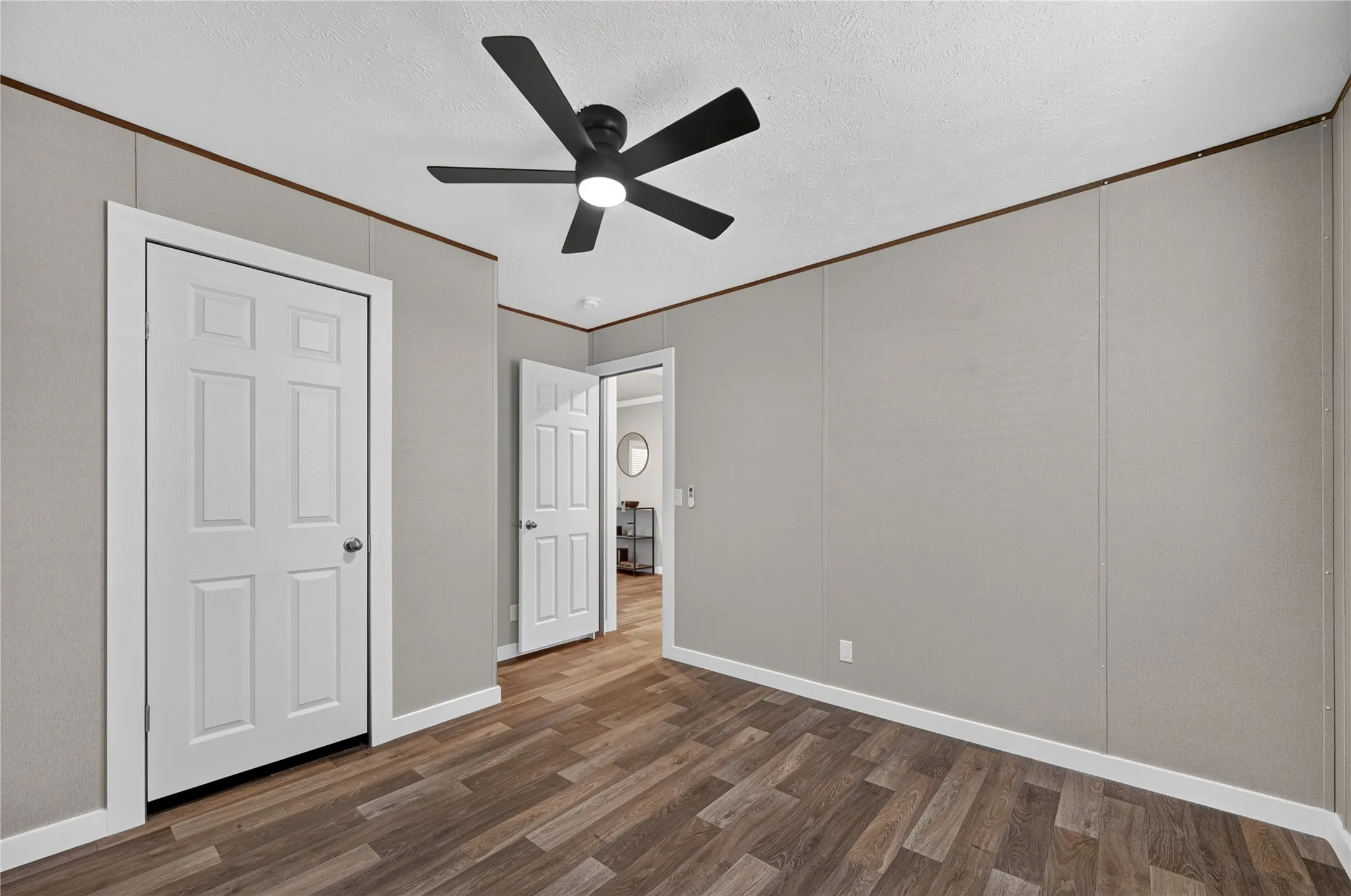 Wood-finish flooring, white paneled doors, ceiling fan with integrated lighting, and neutral wall panels