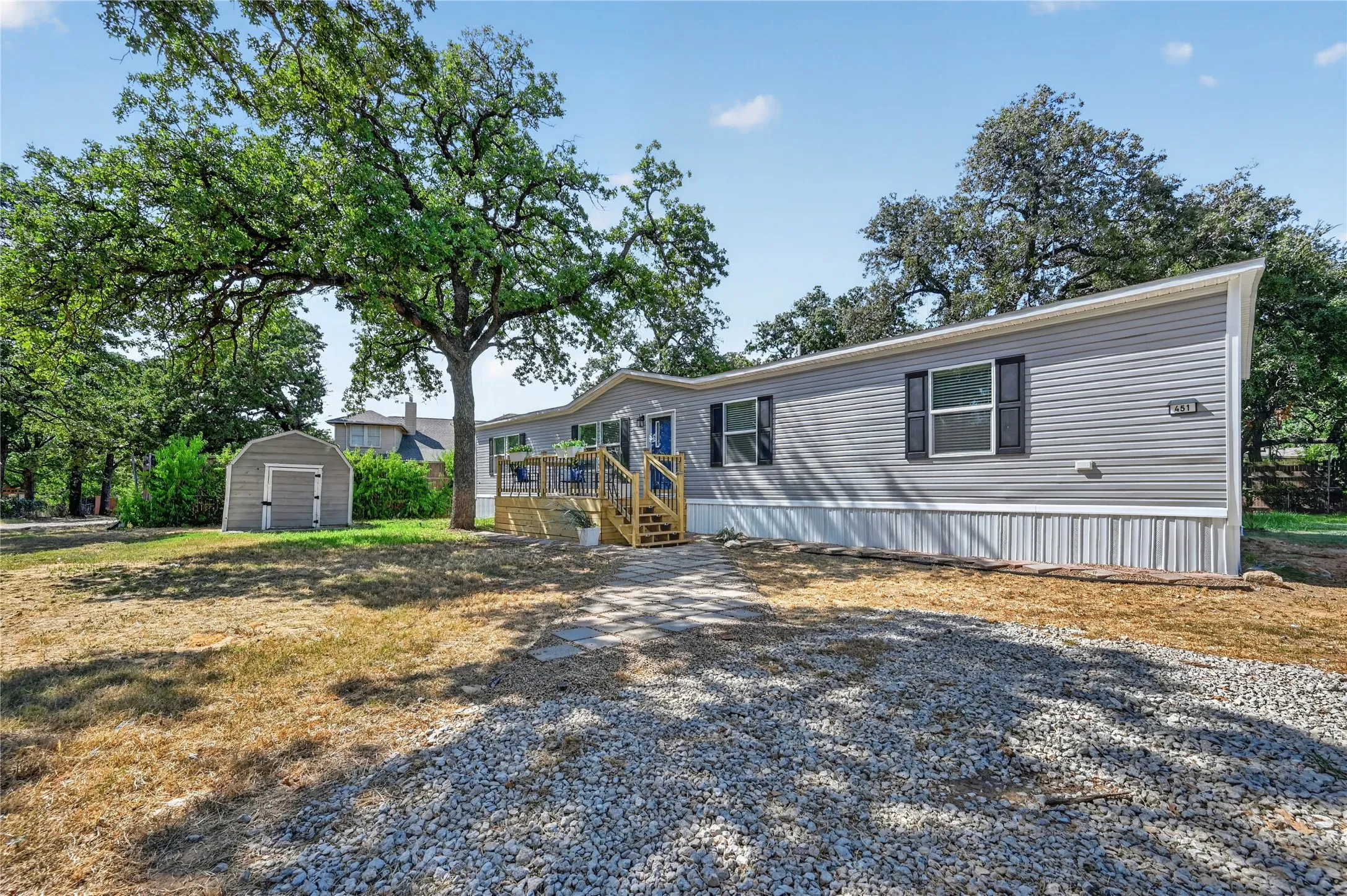 Gray siding exterior with white trim, featuring a gravel driveway and a wooden deck with stairs