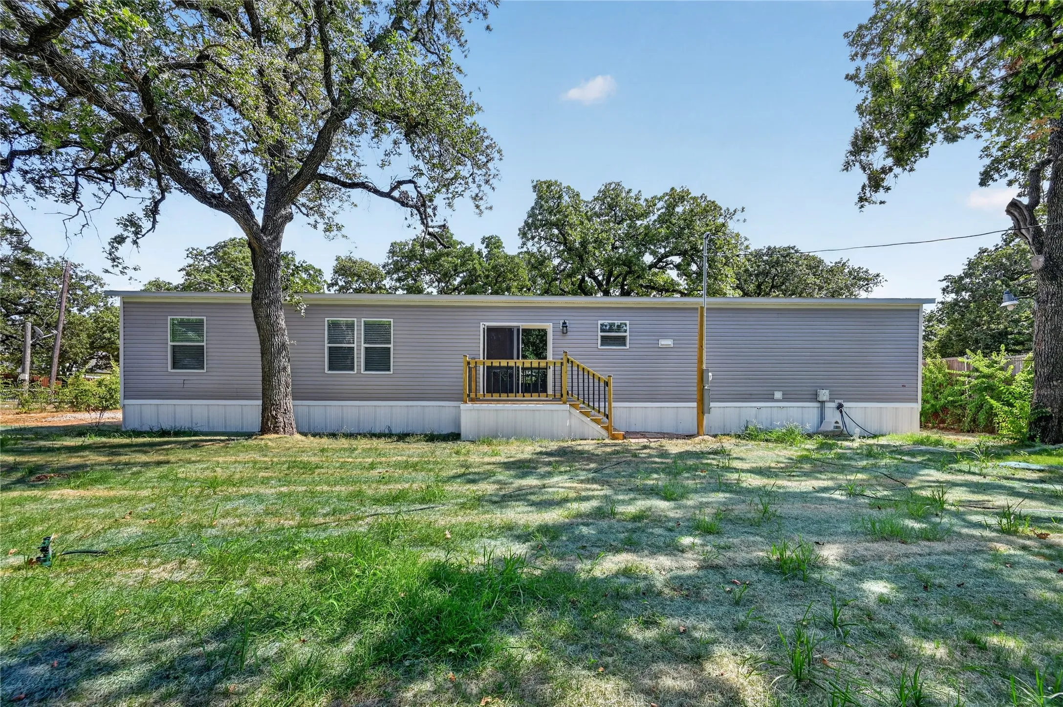 Siding exterior with multiple windows, wooden deck, and a spacious lawn